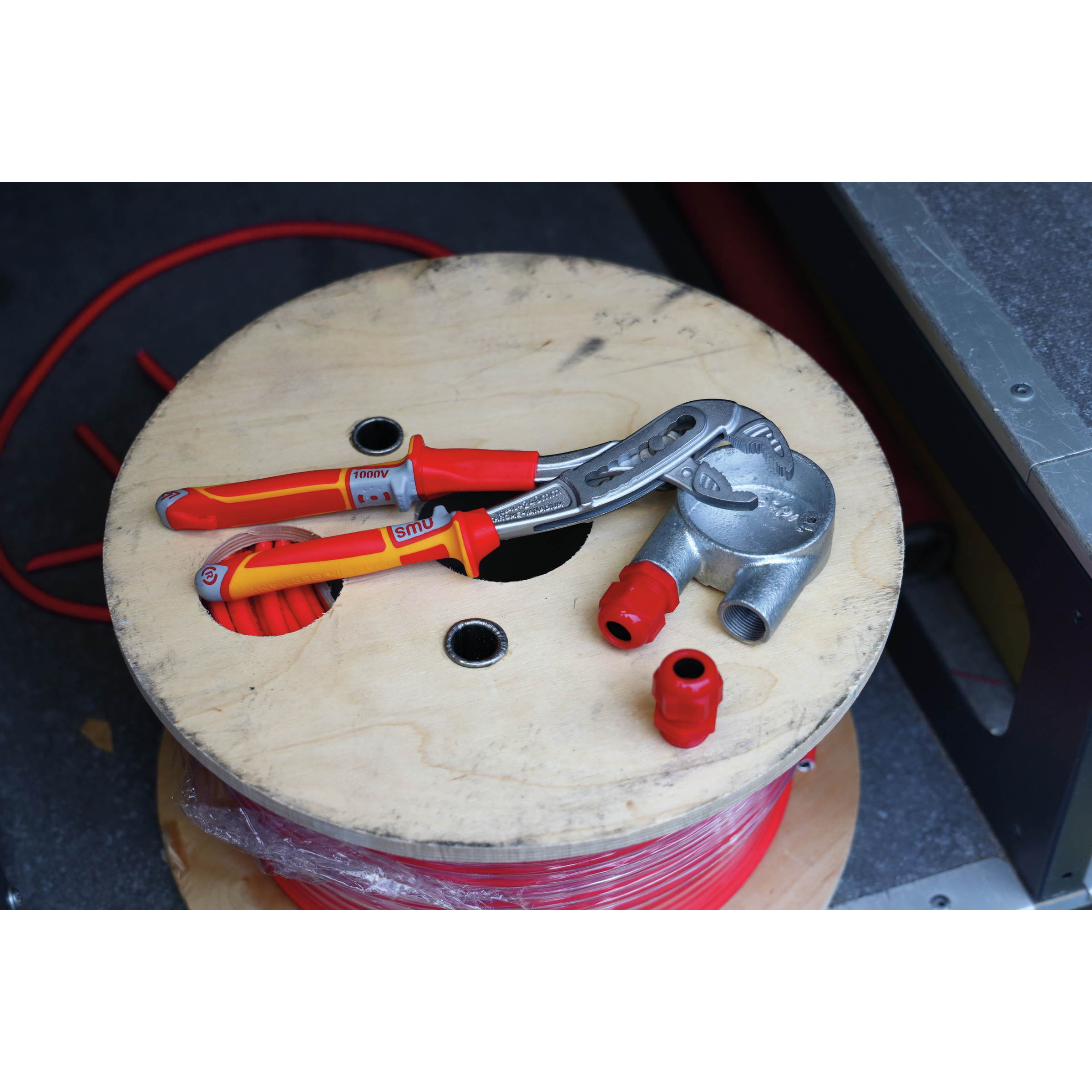 Narzędzia na drewnianej szpuli z czerwonym drutem. Białe tło. Szczypce, obcinak.