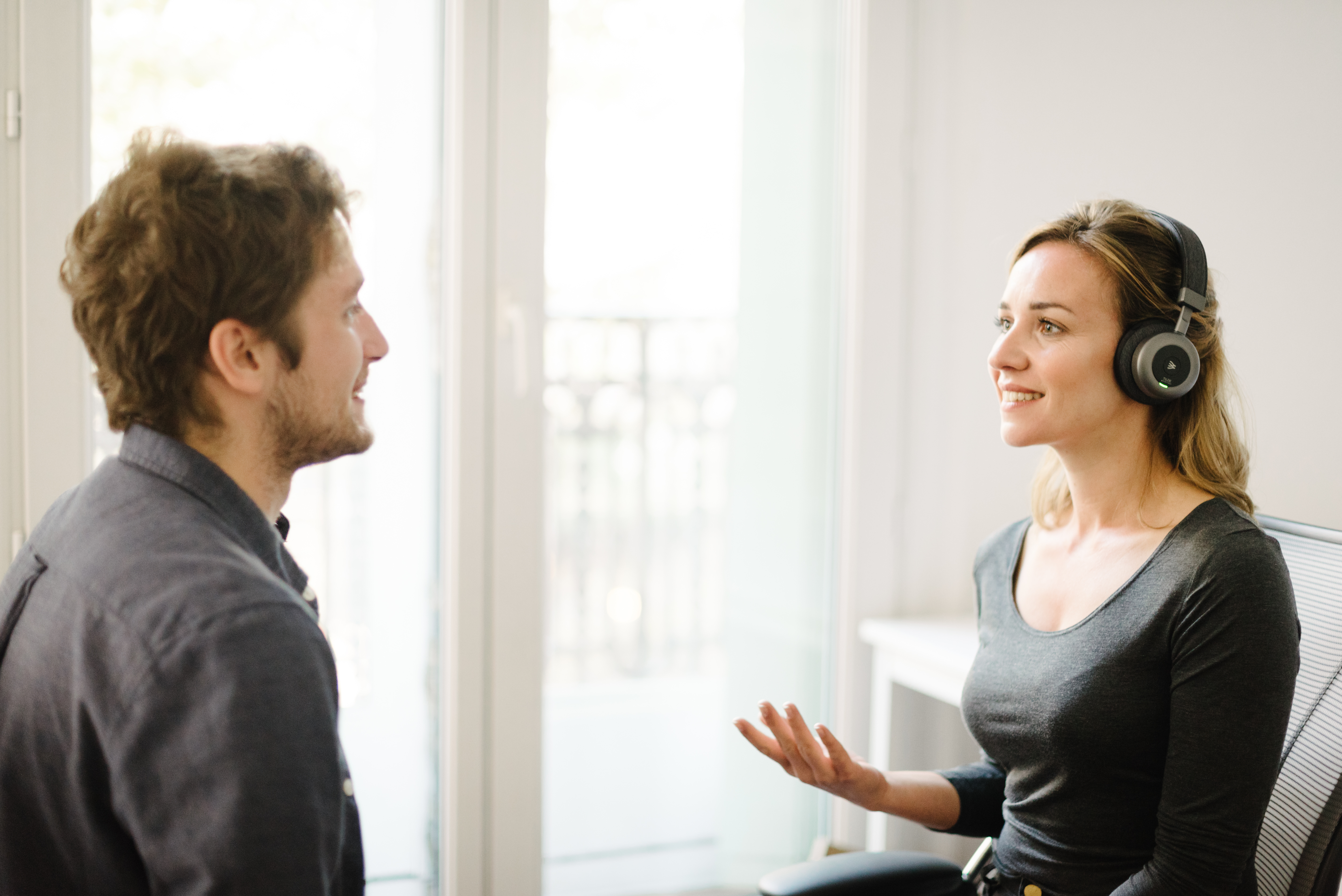 Woman with headphones talking to a man. Office setting with a white table.