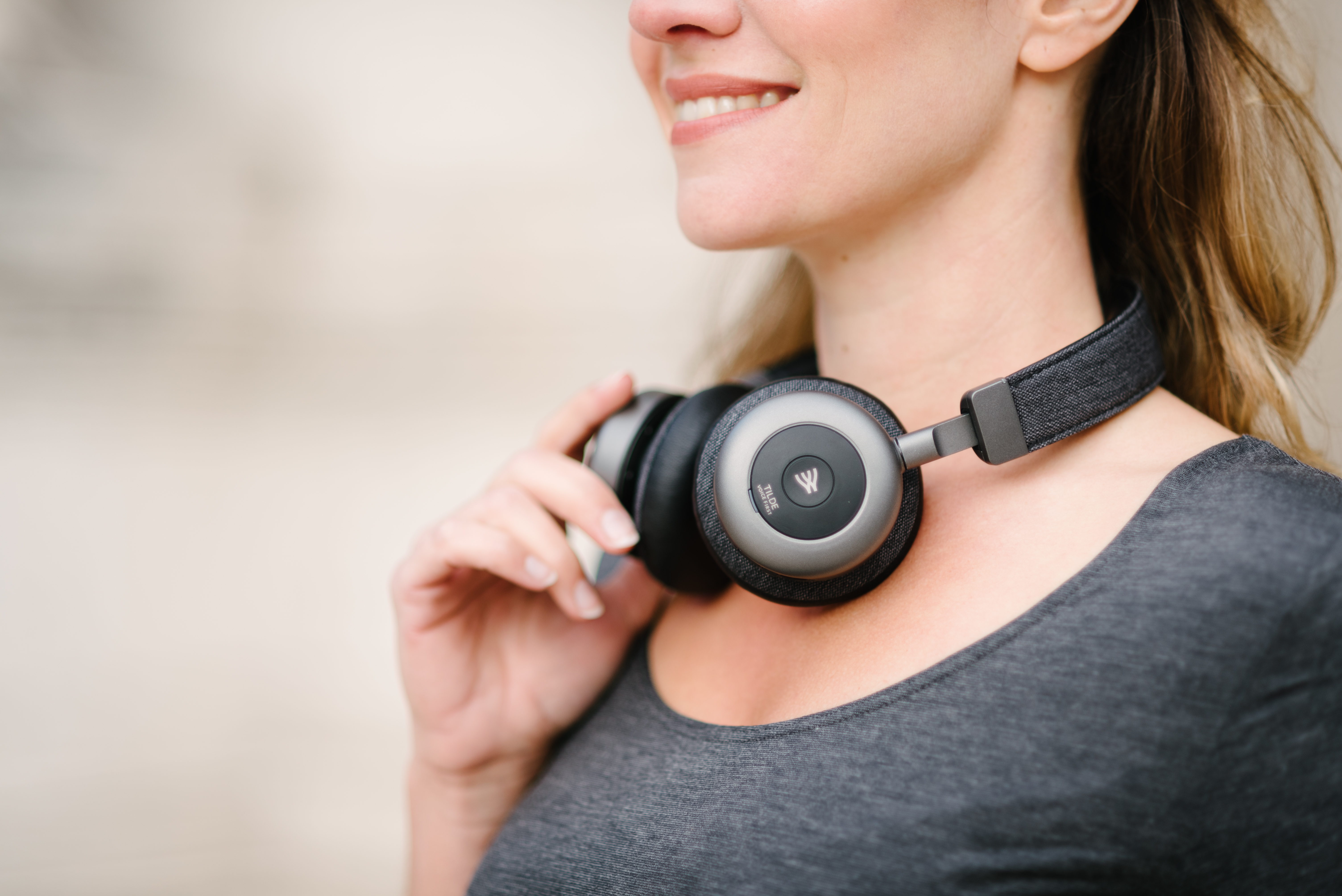 Woman wearing headphones around her neck. She's smiling. Grey t-shirt.