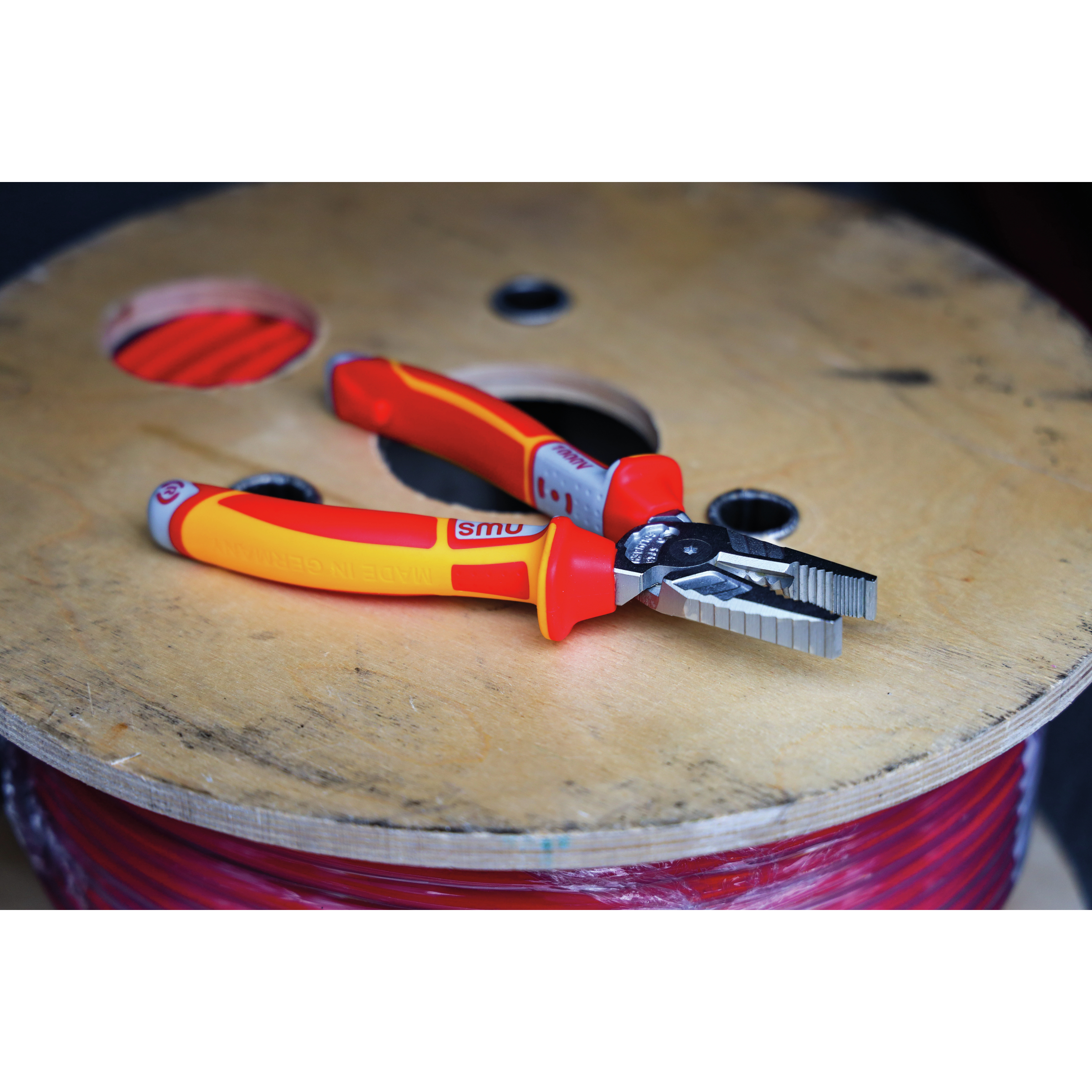 Szczypce na drewnianej szpuli. Czerwono-żółte uchwyty, srebrne szczęki. Tło drewnianej szpuli.