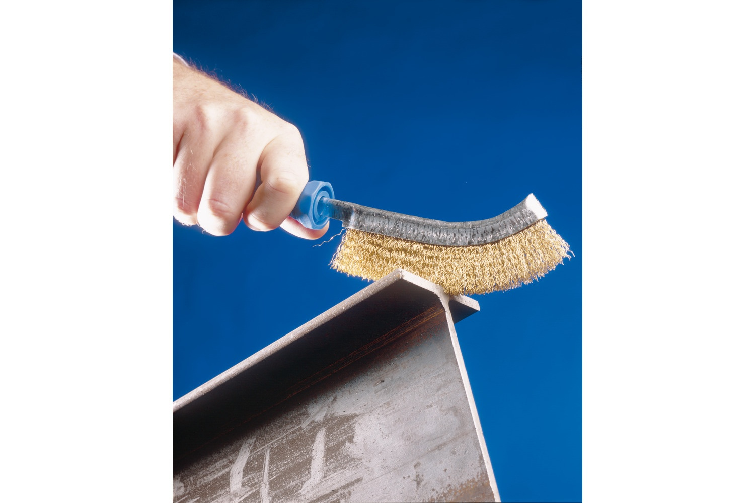 Eine Hand verwendet eine Drahtbürste an einem Metallträger. Die Bürste ist blau und hat Messingborsten.