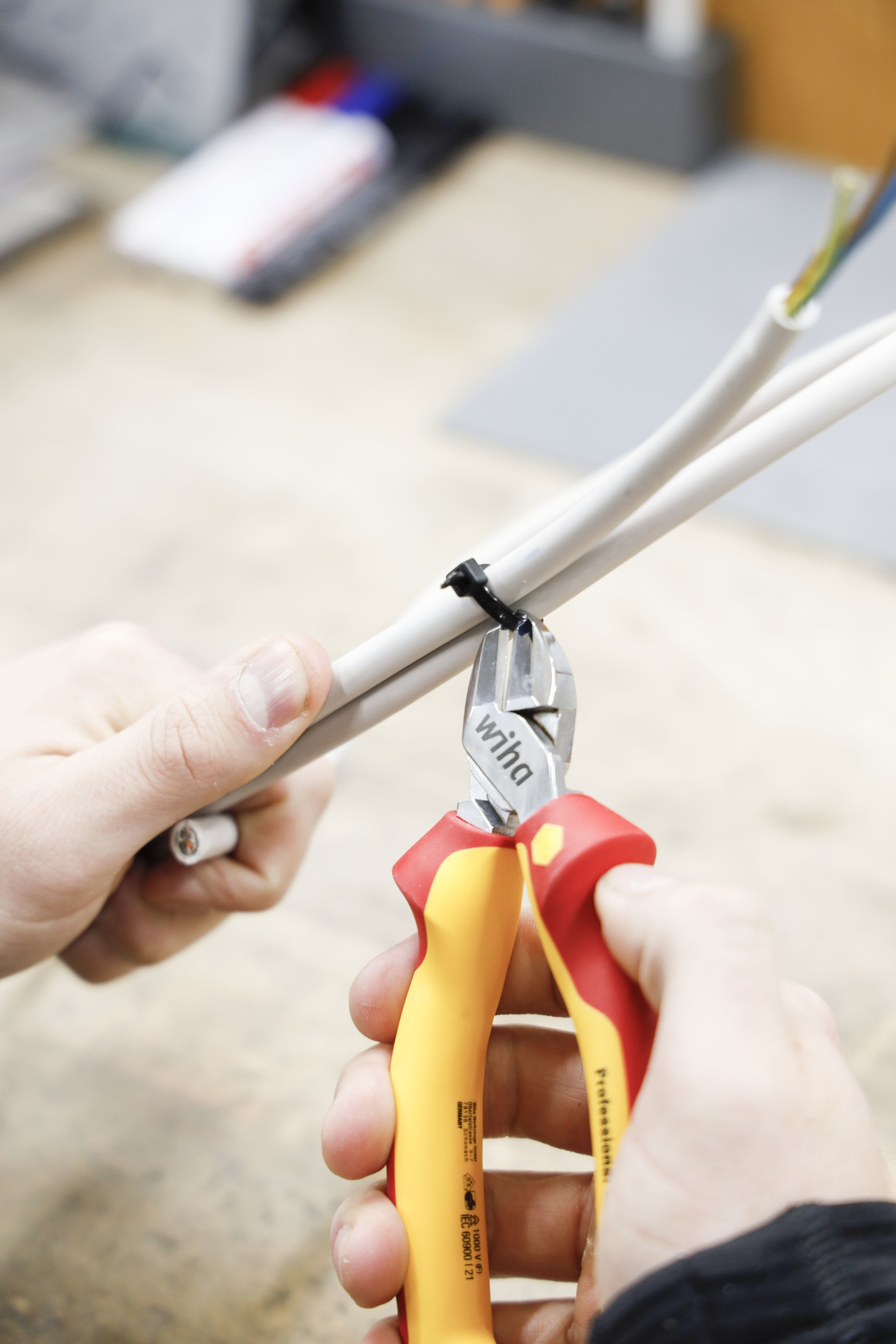 Zbliżenie szczypiec przecinających opaskę. Widoczne białe kable i kolorowe przewody.