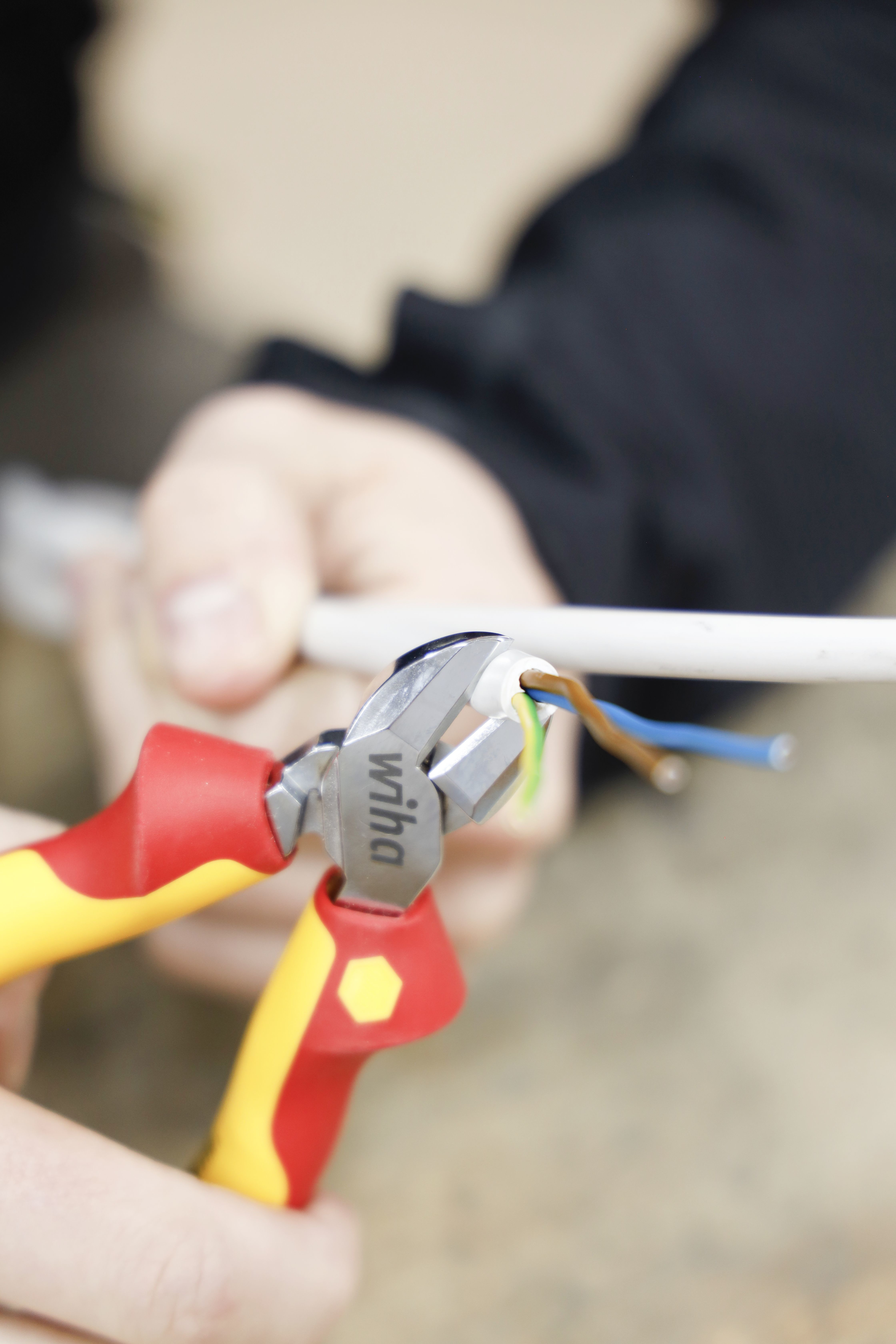 Szczypce przecinają przewód. Przewody są widoczne w różnych kolorach. Zbliżenie z drewnianym tłem.