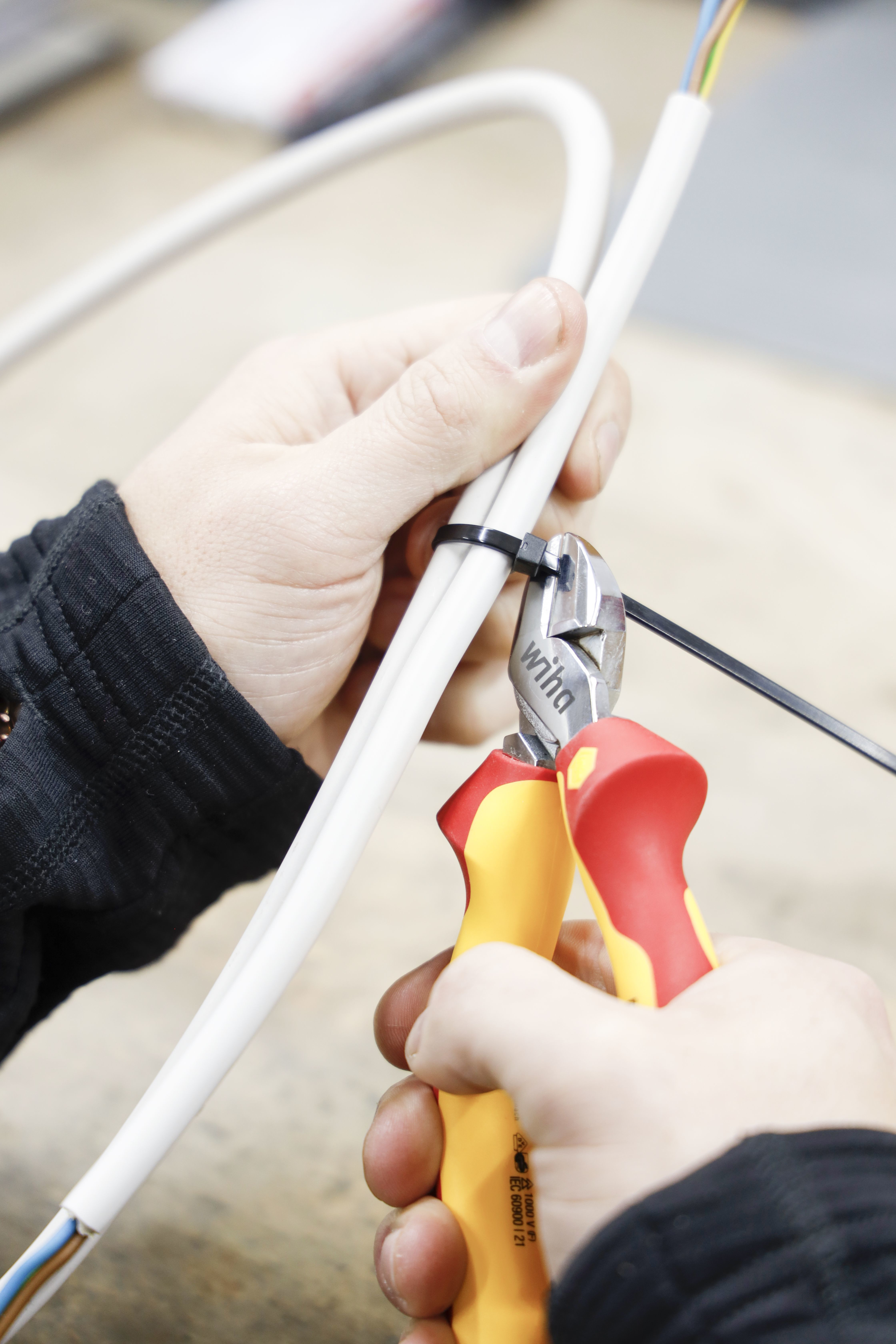 Szczypce przecinają czarną opaskę na białych kablach. Przewody są widoczne. Zbliżenie.