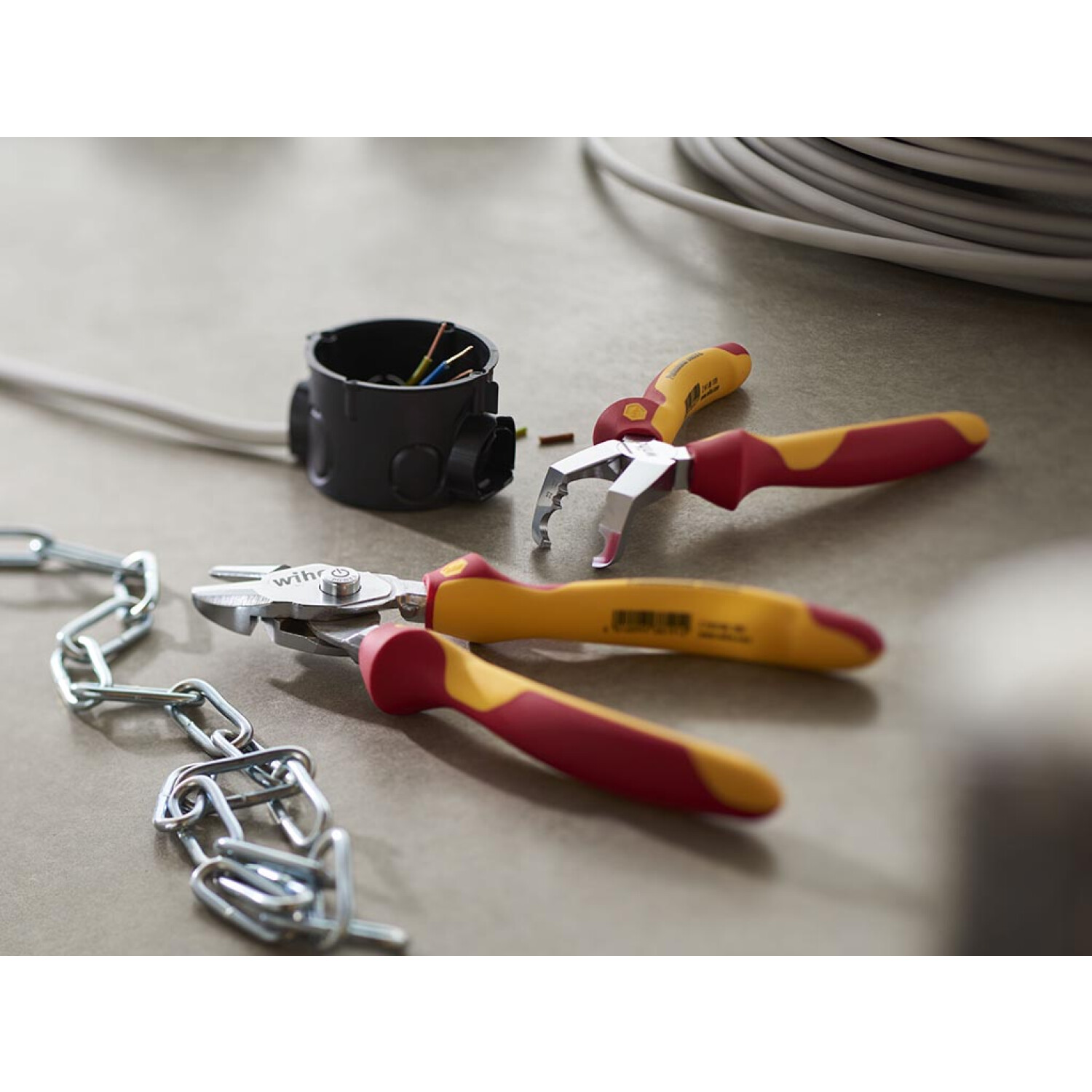Narzędzia na szarej powierzchni: obcinak do drutu, szczypce, łańcuch, puszka połączeniowa i przewody.