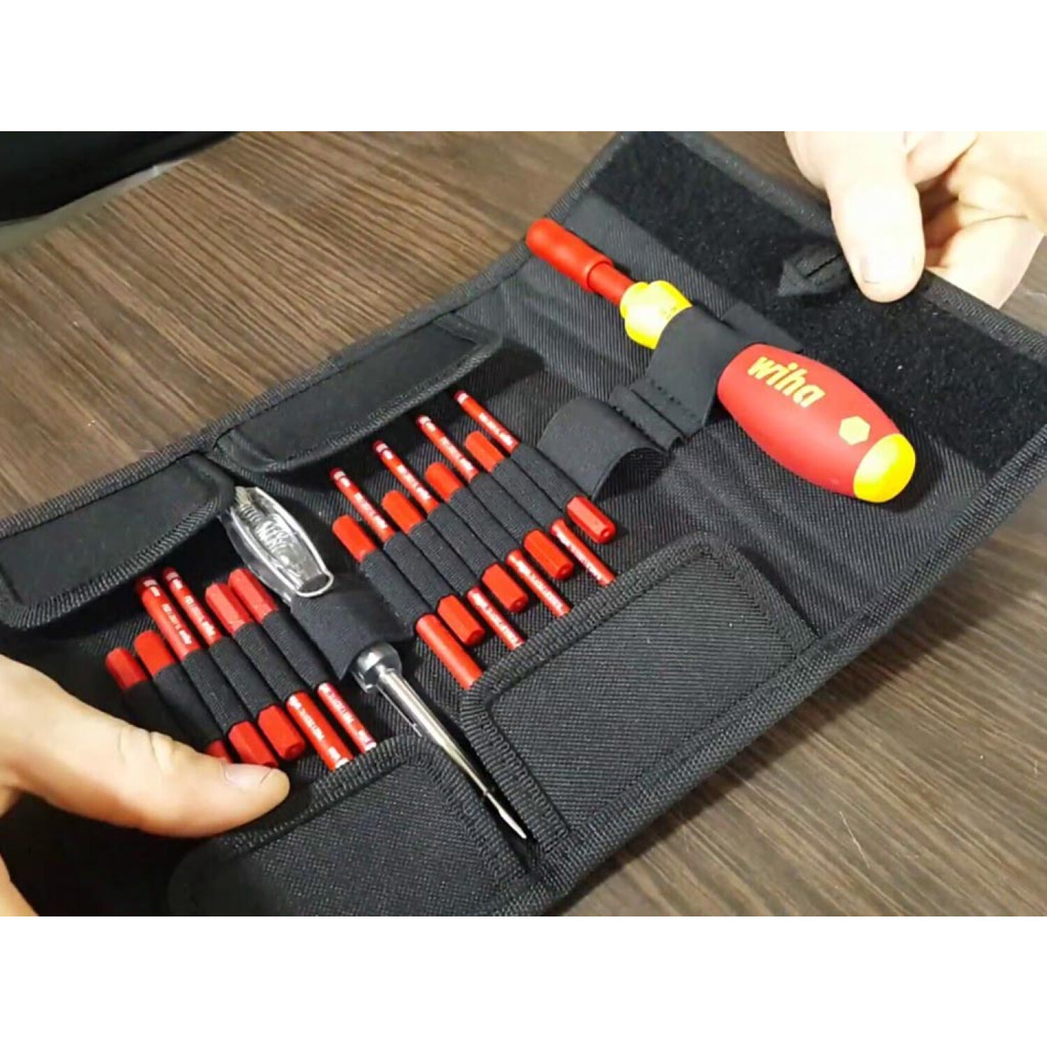 Ręce trzymające czarny zwój narzędzi z czerwonymi śrubokrętami Wiha.