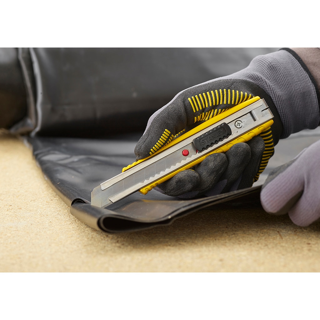 Person schneidet mit einem gelb-schwarzen Cuttermesser ein schwarzes Blatt. Trägt Handschuhe.