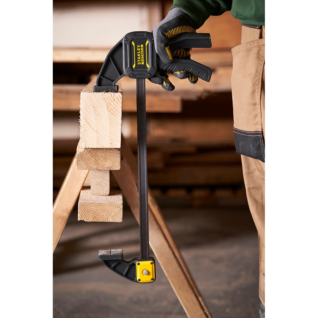Una persona usando una abrazadera para sujetar dos trozos de madera. Fondo de madera.