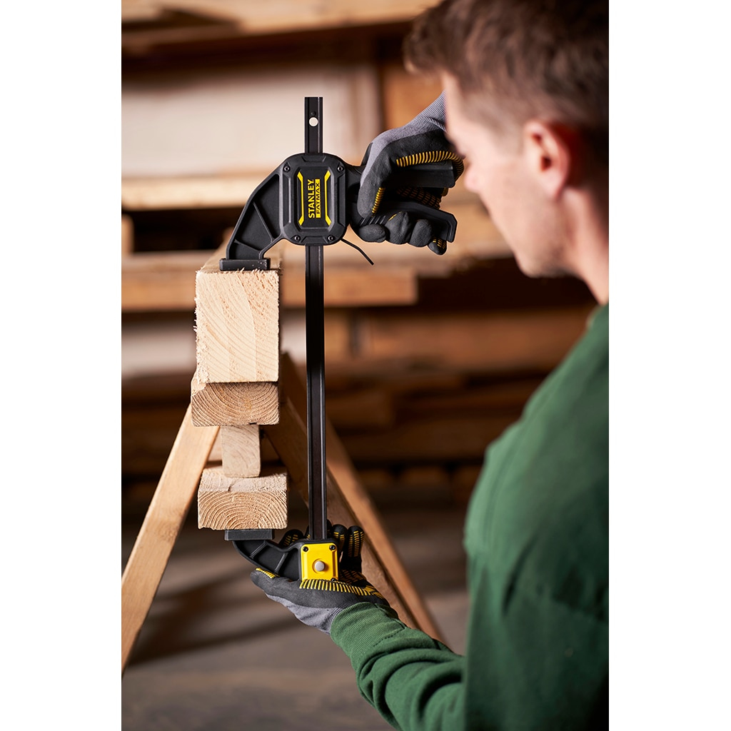 Una persona usando una abrazadera para sujetar dos trozos de madera. Fondo de madera.