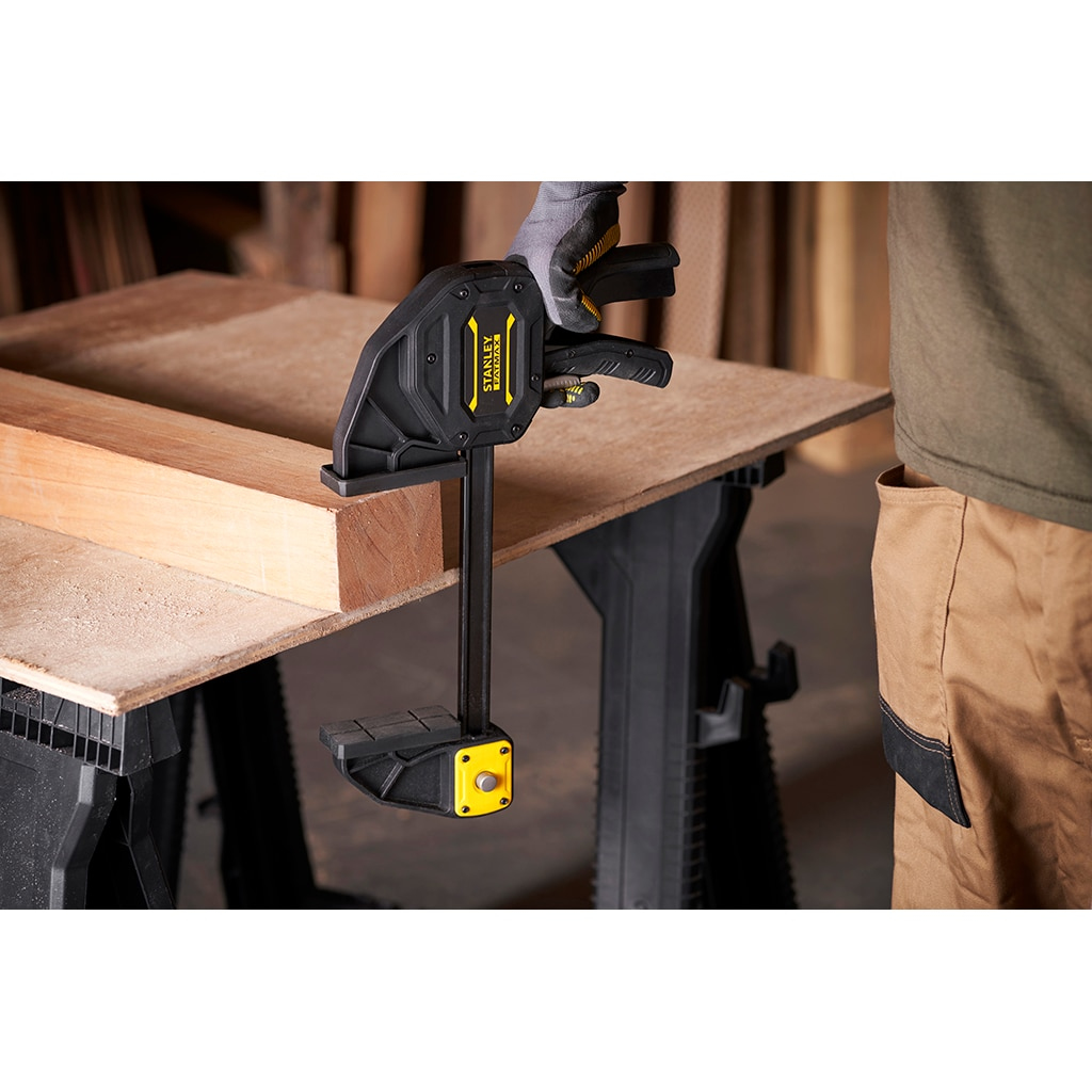 Abrazadera sujetando madera sobre una mesa. Una persona está trabajando. El fondo está desenfocado.