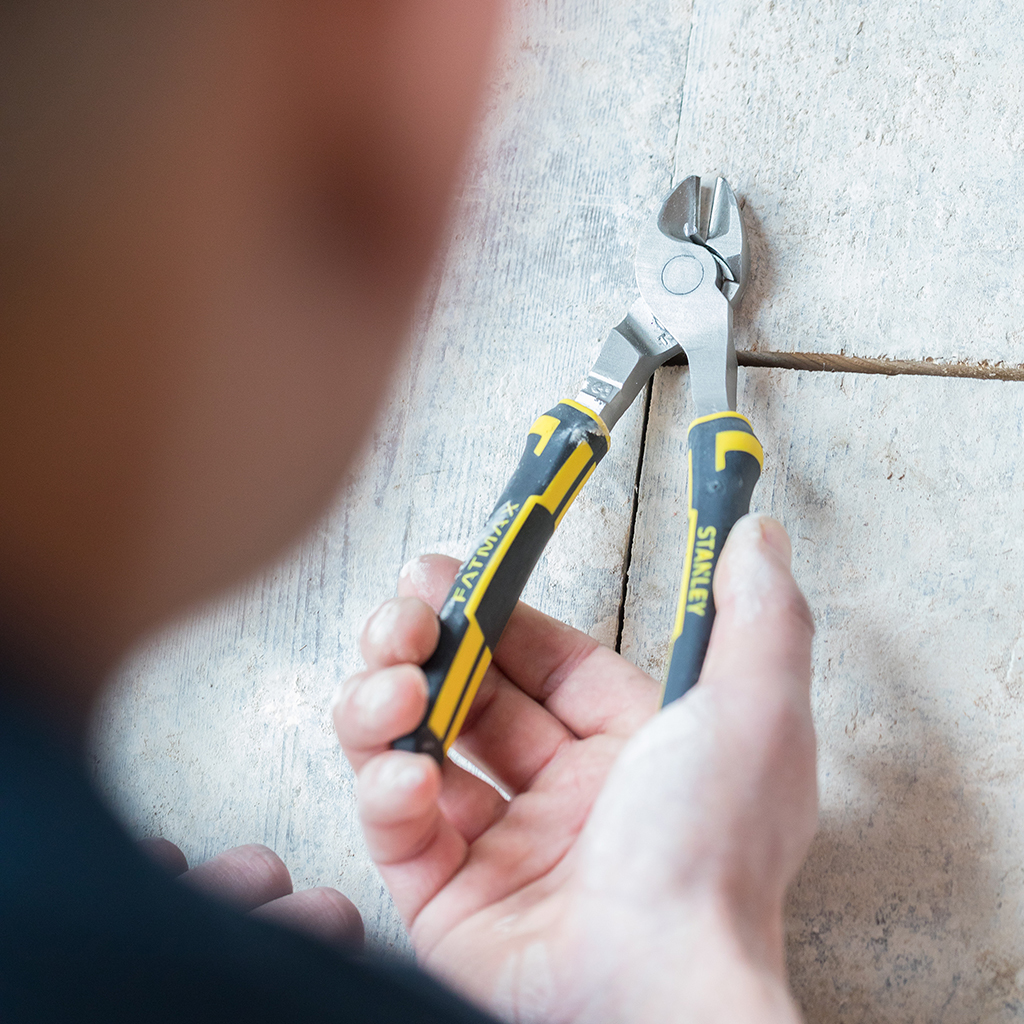 Person hält Zange, schneidet etwas an einer hellen Wand. Zange mit 'FATMAX' beschriftet.