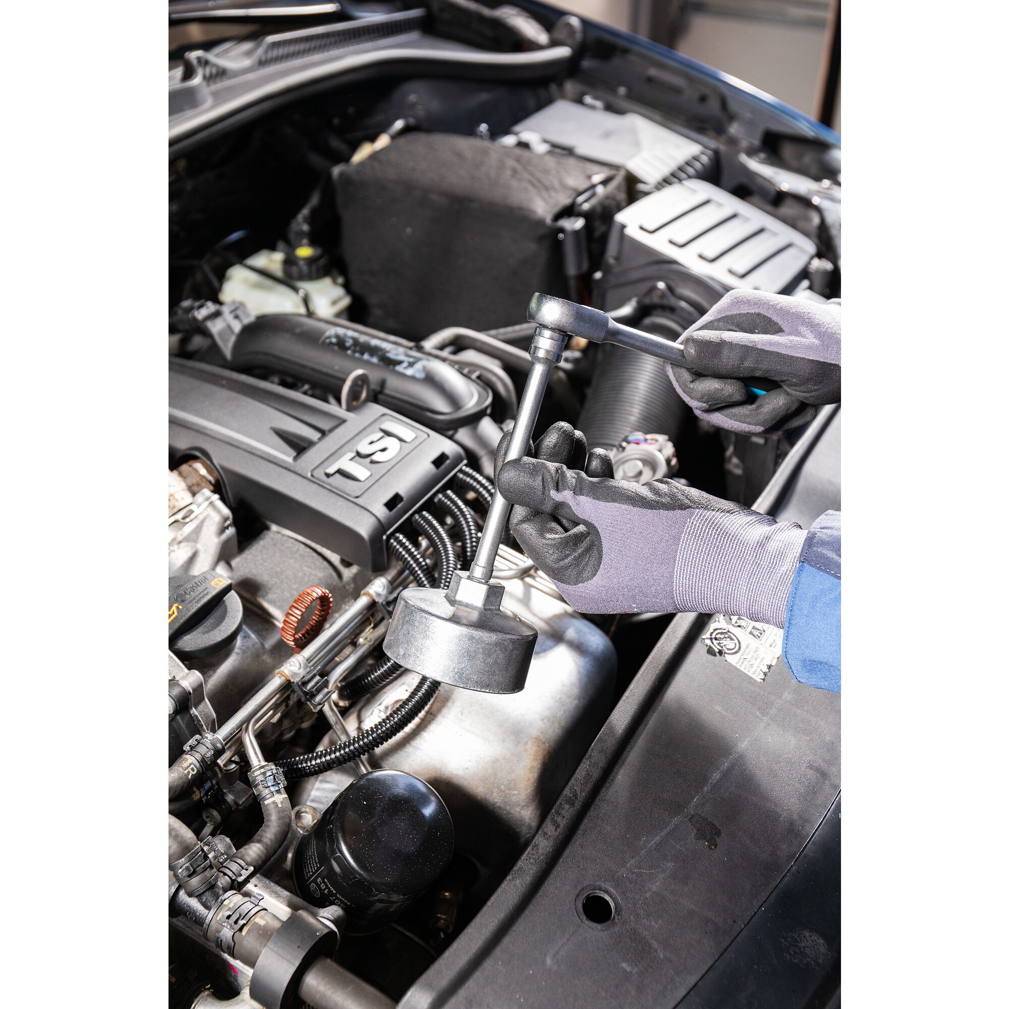 Manos usando una llave para quitar el filtro de aceite de un motor de coche.