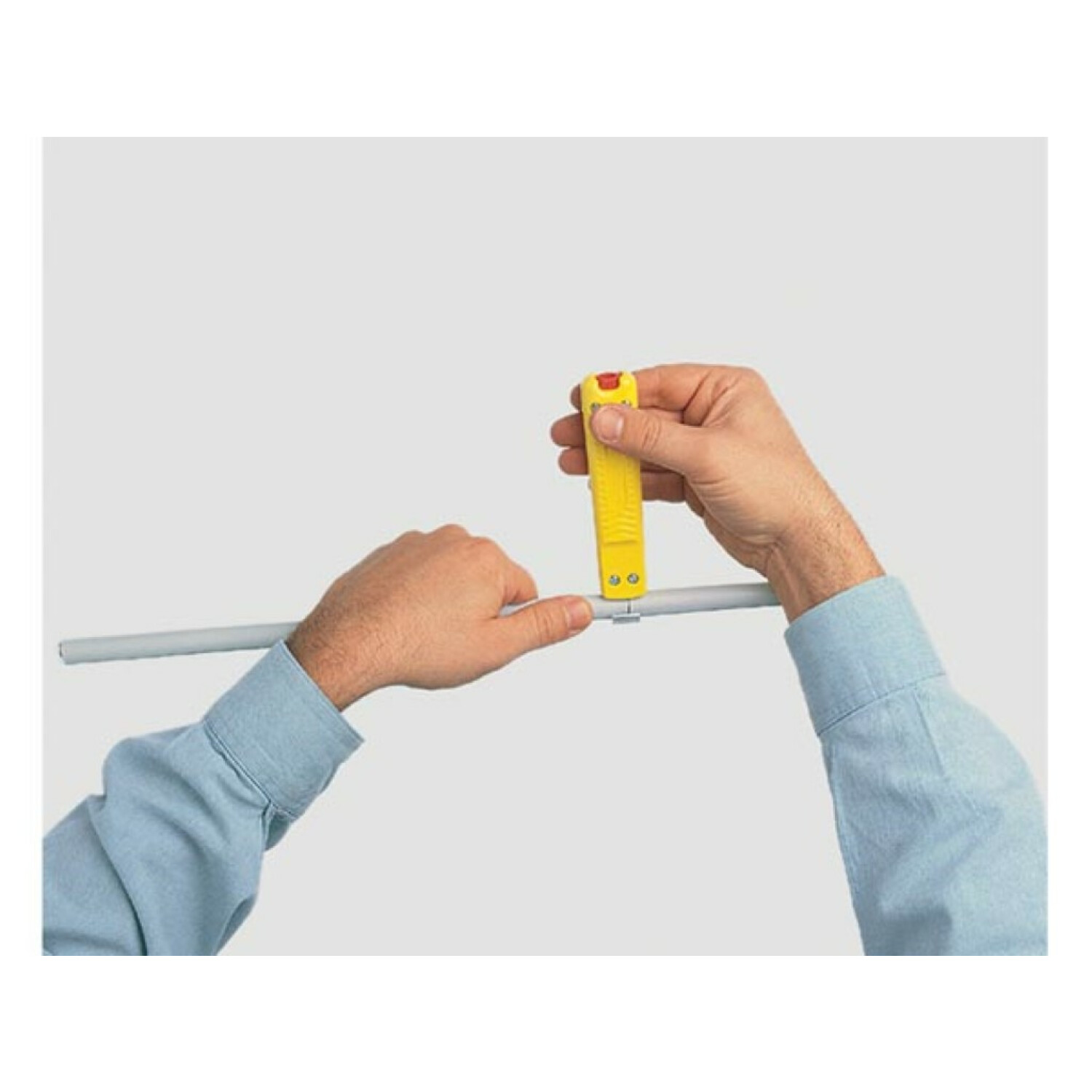 Ręce używające żółtego narzędzia na szarej rurze. Jasnoszare tło.