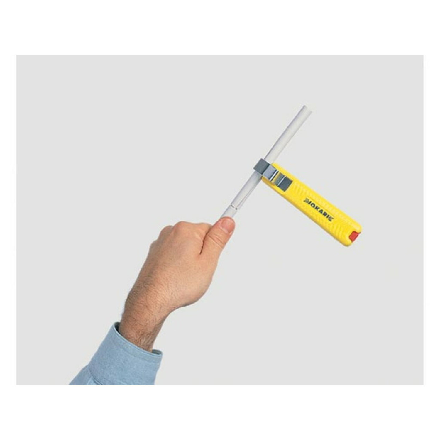 Ręka trzymająca żółte narzędzie na szarej rurze. Jasnoszare tło.