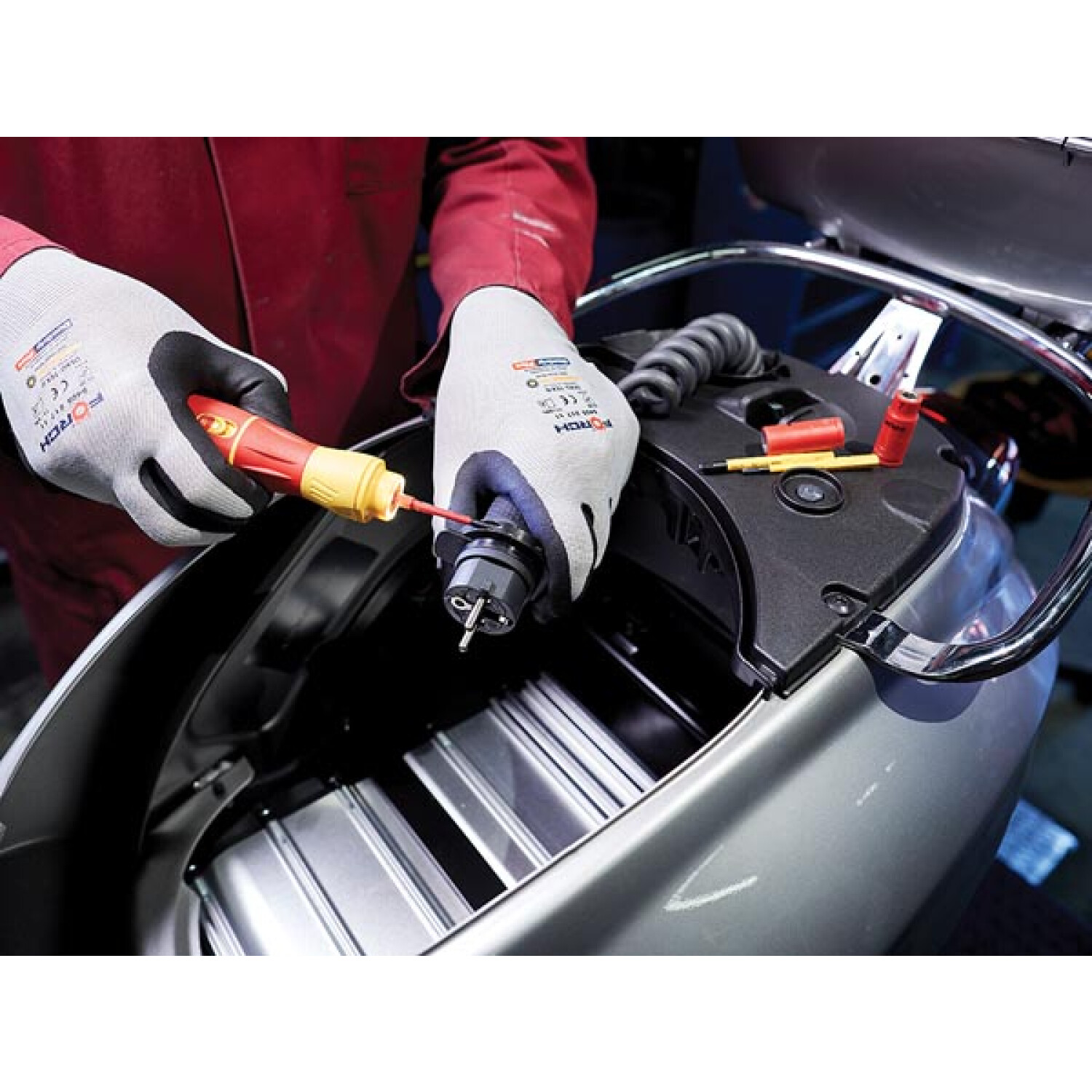 Osoba w rękawicach używa śrubokręta do pracy przy komponencie elektrycznym skutera. Widoczne są narzędzia i części skutera.