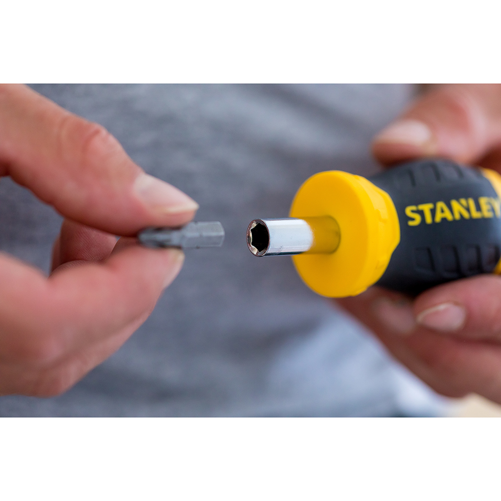 Una mano insertando una punta en un destornillador multibit Stanley amarillo y negro, sobre fondo borroso.