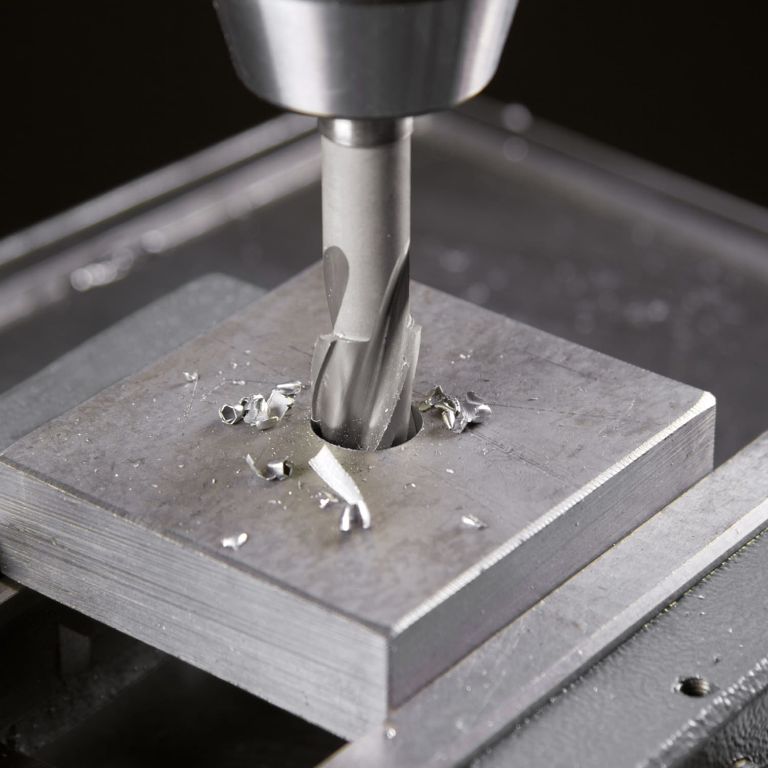 Wiertło robiące otwór w metalowej płycie, wióry wokół, zbliżenie.