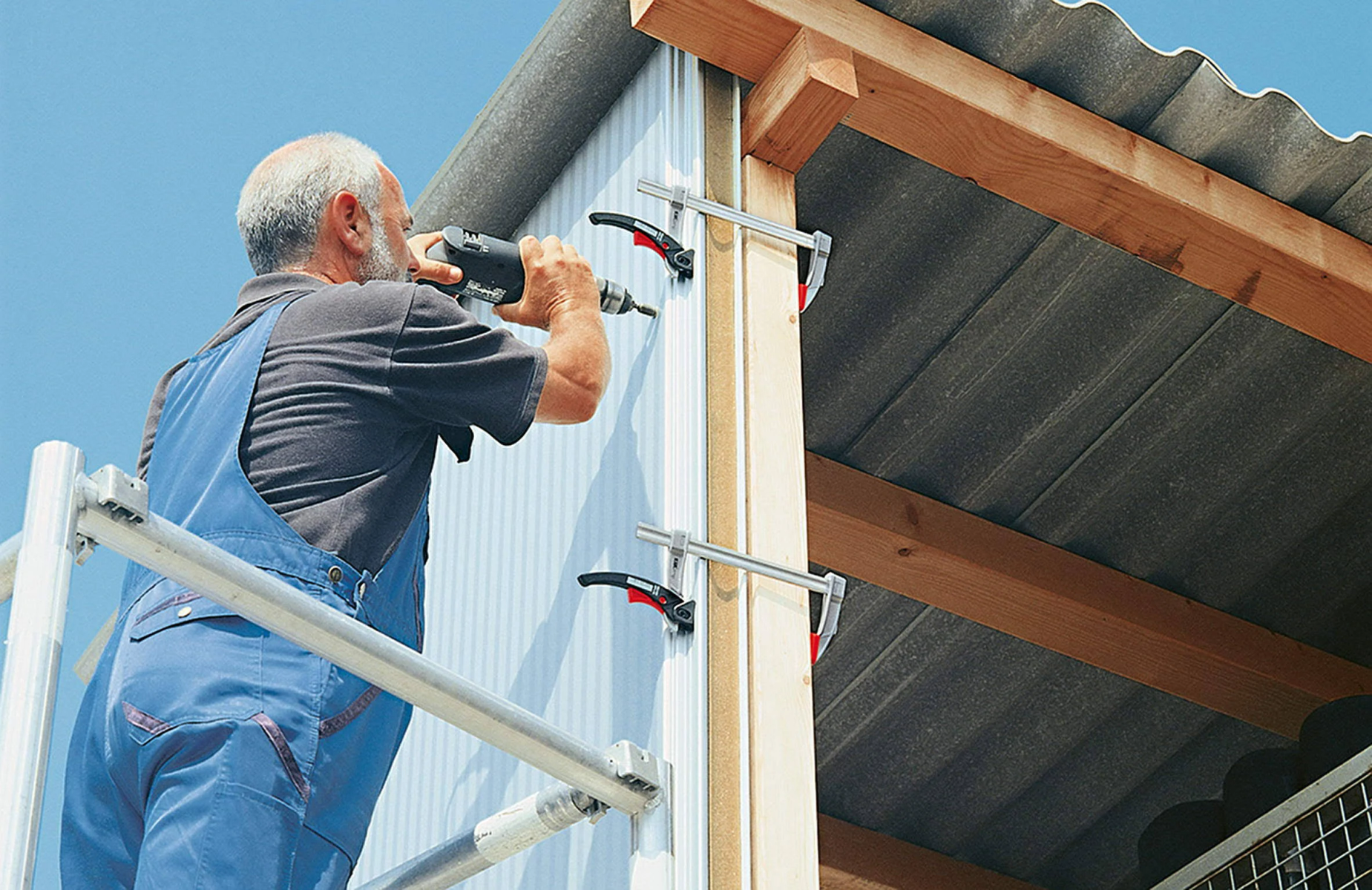 Un hombre usa un taladro para fijar tornillos. Utiliza abrazaderas para sujetar la madera en su lugar.