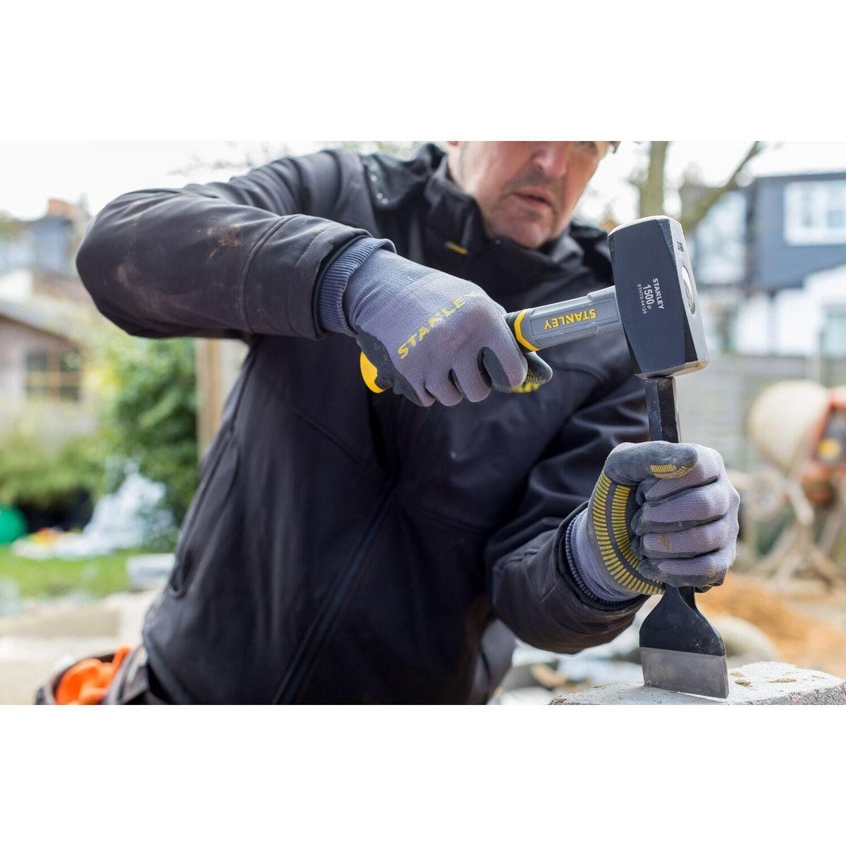 Ein Mann mit Handschuhen benutzt einen Vorschlaghammer und Meißel, um einen Steinblock auf einer Baustelle zu zerbrechen.