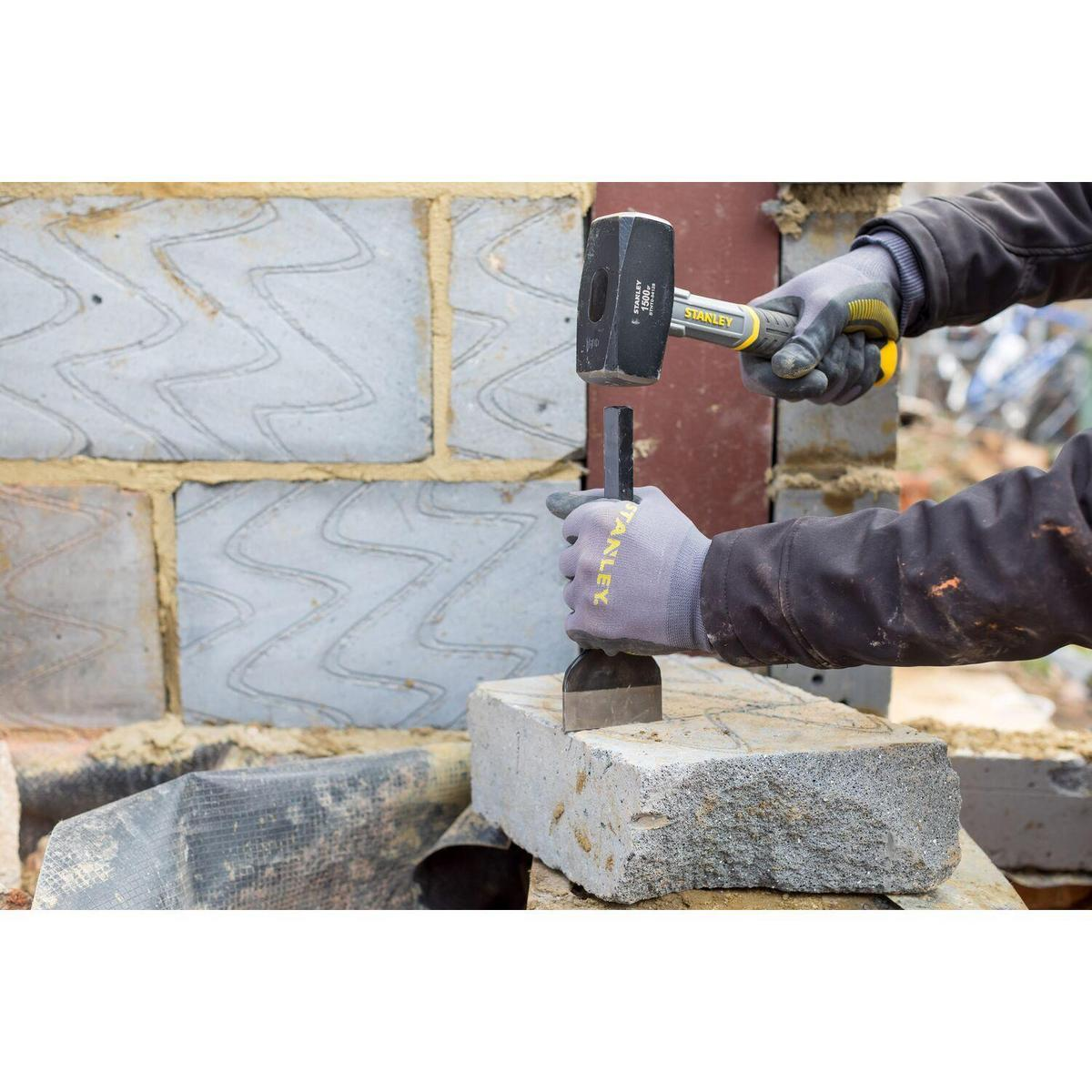 Hände benutzen einen Vorschlaghammer und Meißel, um einen Steinblock zu spalten, der auf einer Backsteinmauer platziert ist. Bauszene.