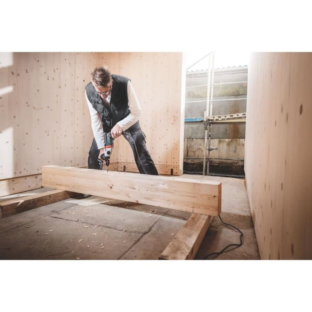 Osoba wiercąca drewnianą belkę w pomieszczeniu z drewnianymi ścianami.