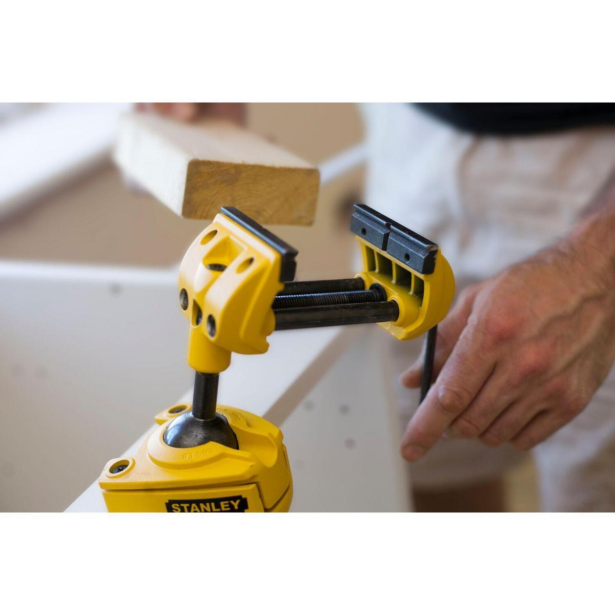 Gelber Stanley-Schraubstock klemmt Holz, Hand hält das Holz, weißer Hintergrund.