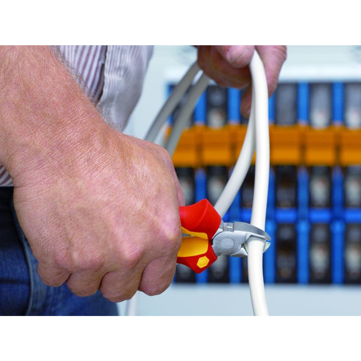 Osoba używająca czerwono-żółtych szczypiec do cięcia białego kabla. Widok z bliska.