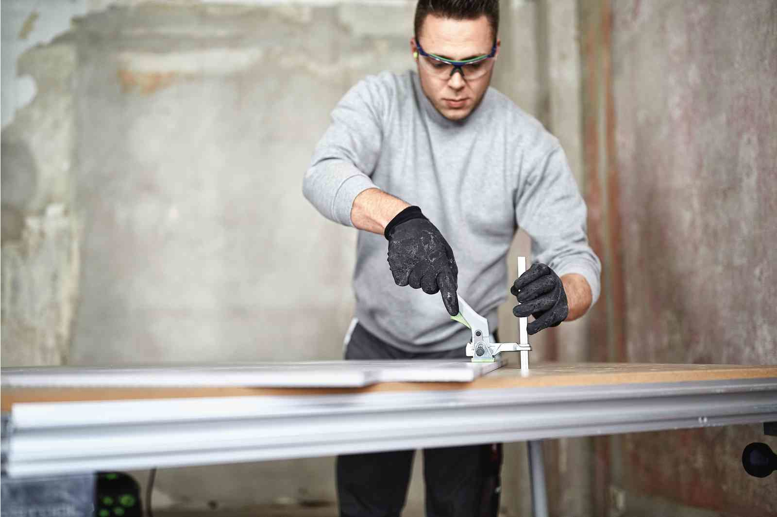 Mężczyzna używa zacisku do cięcia deski. Szara i biała ściana w tle.