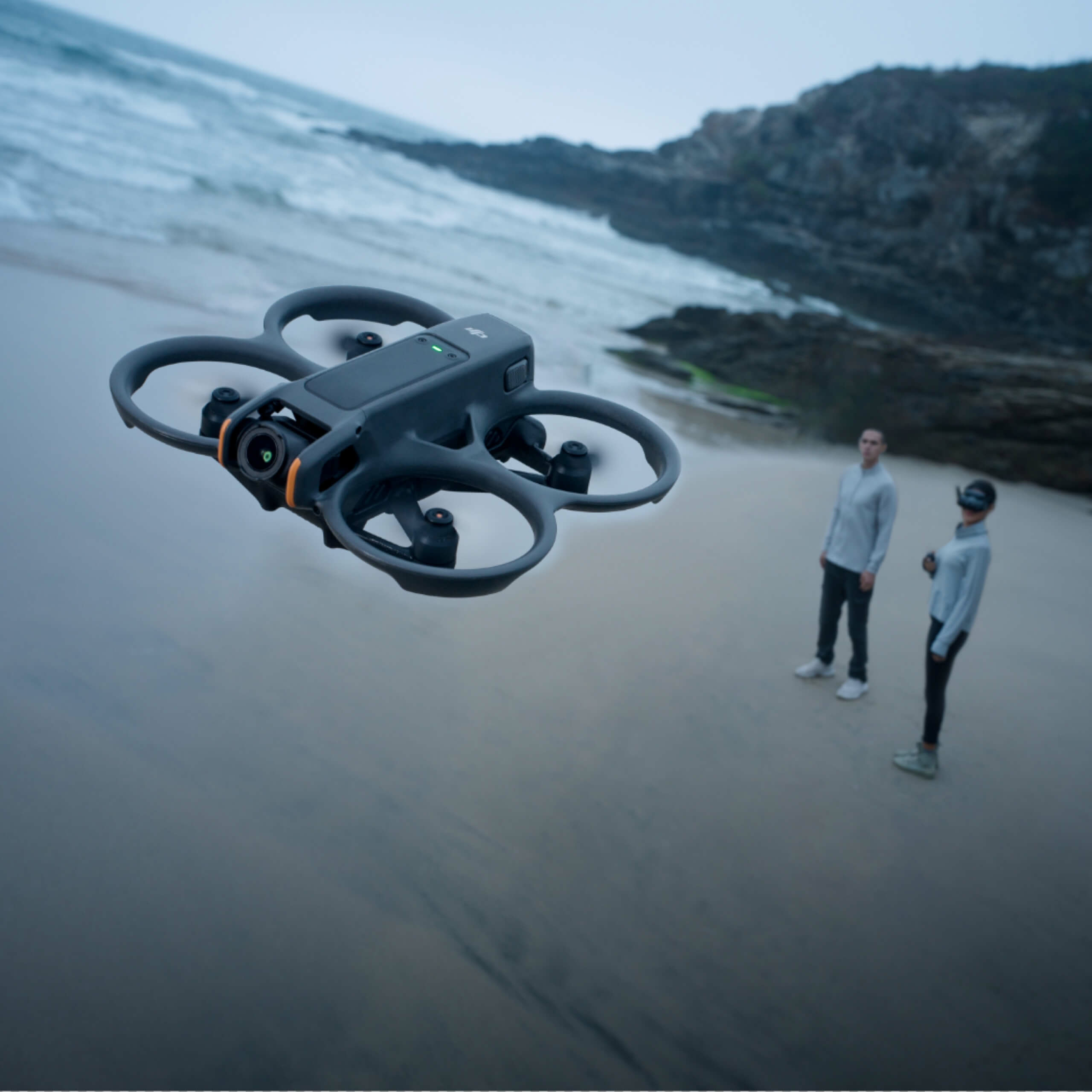 Dron leci nad plażą z dwiema osobami w tle.