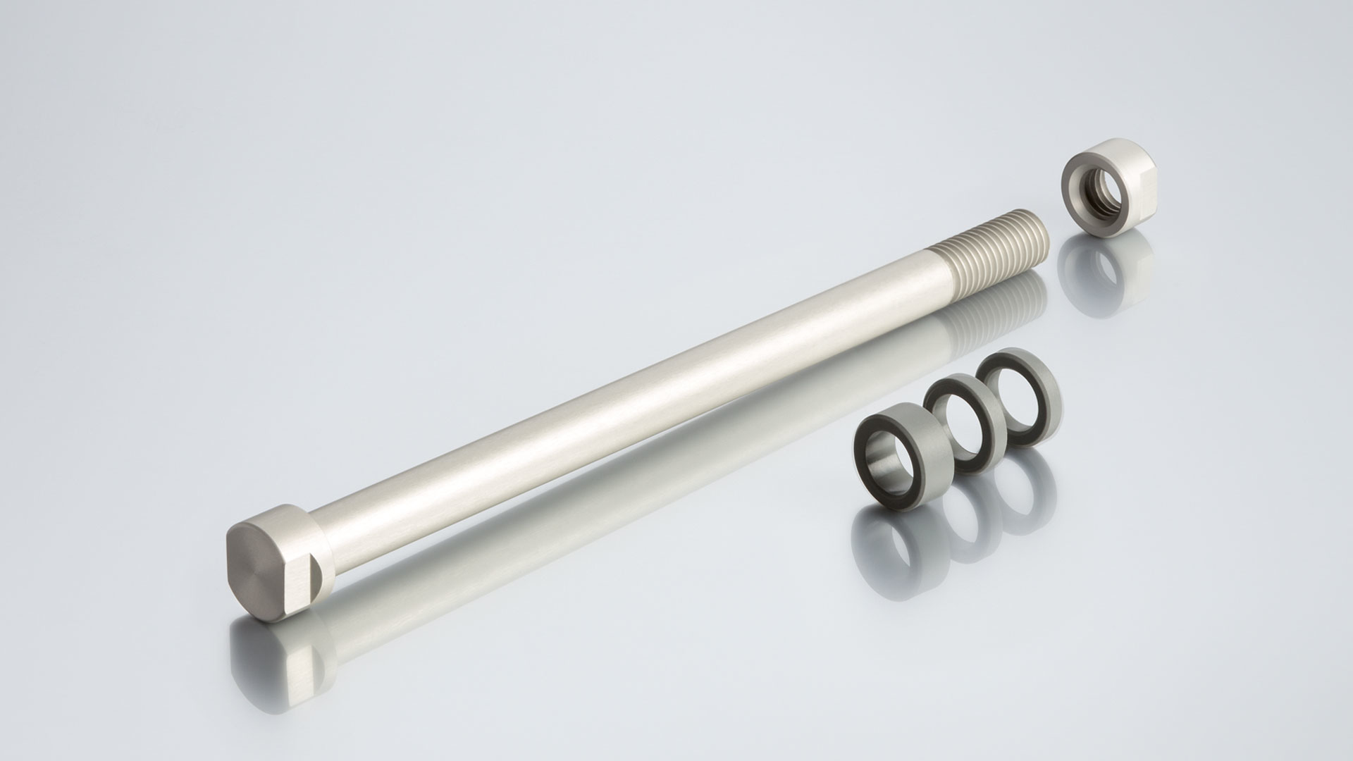 Bullone metallico con dado e rondelle su una superficie riflettente.