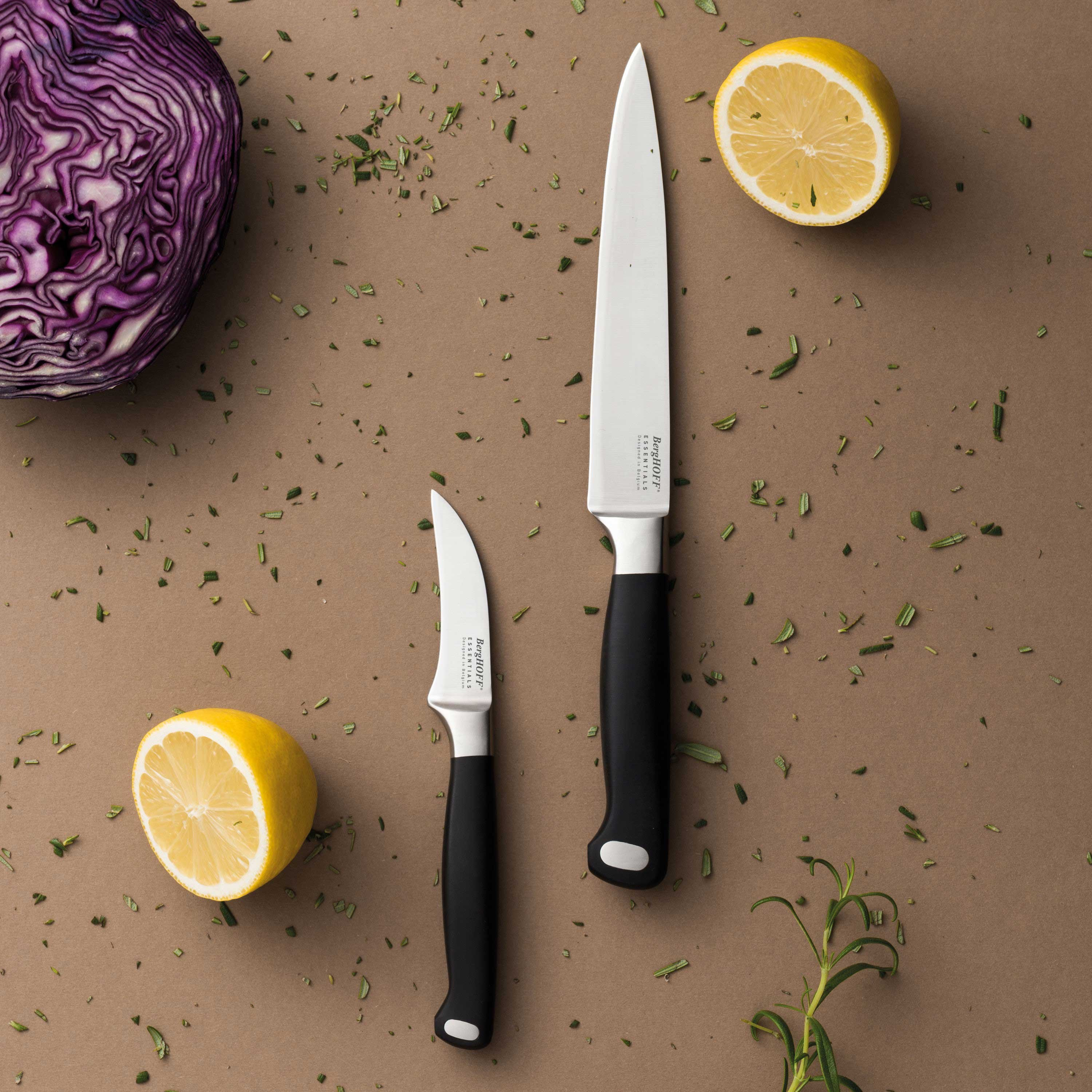 Two knives, two lemon halves, and red cabbage on a brown surface. Herbs are scattered around.