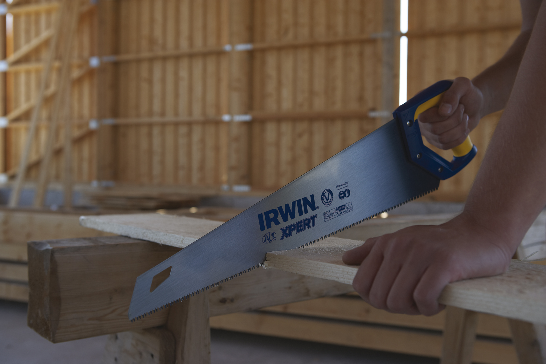 Eine Person sägt mit einer Handsäge Holz. Die Säge ist eine IRWIN XPERT Säge mit blauem Griff.