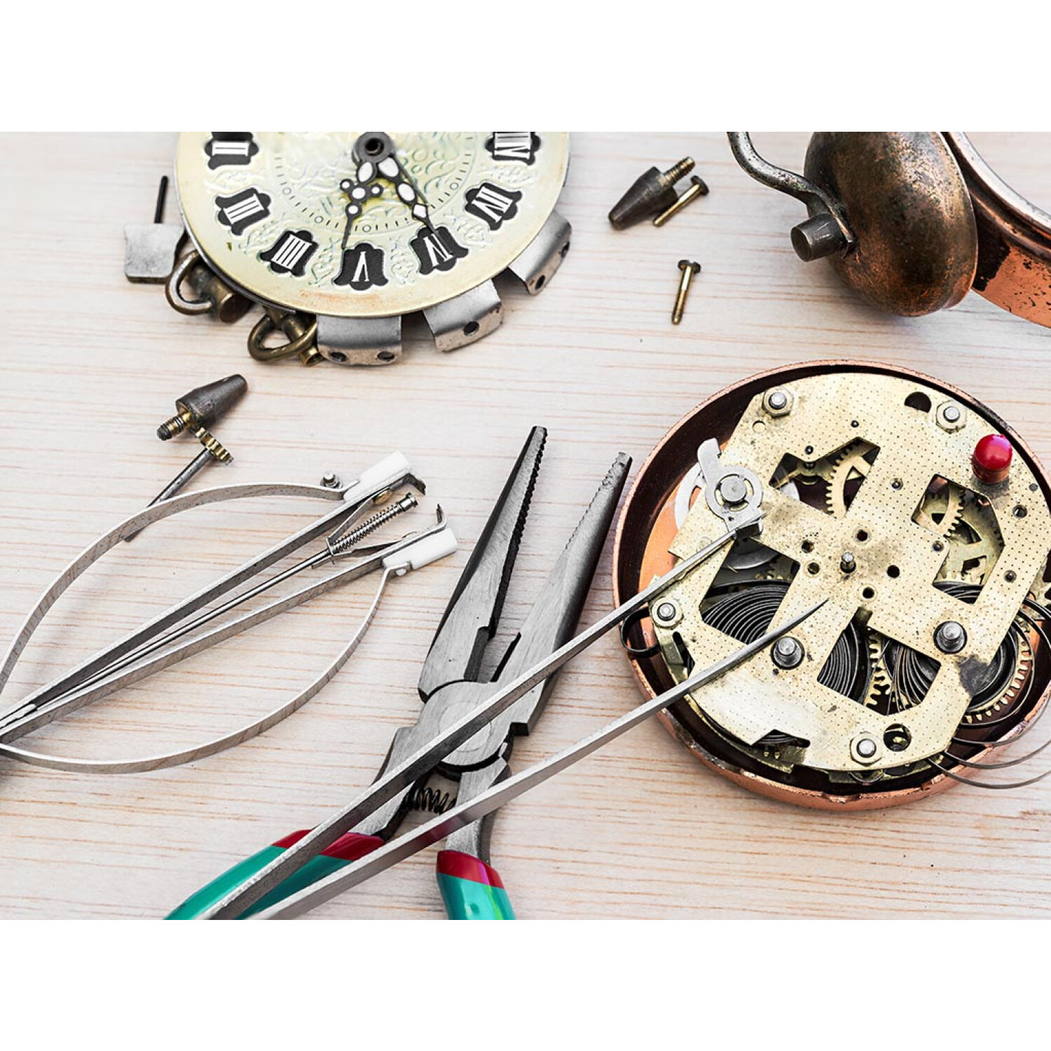 Werkzeuge und Teile zur Reparatur einer Uhr auf einer hellen Holzoberfläche.