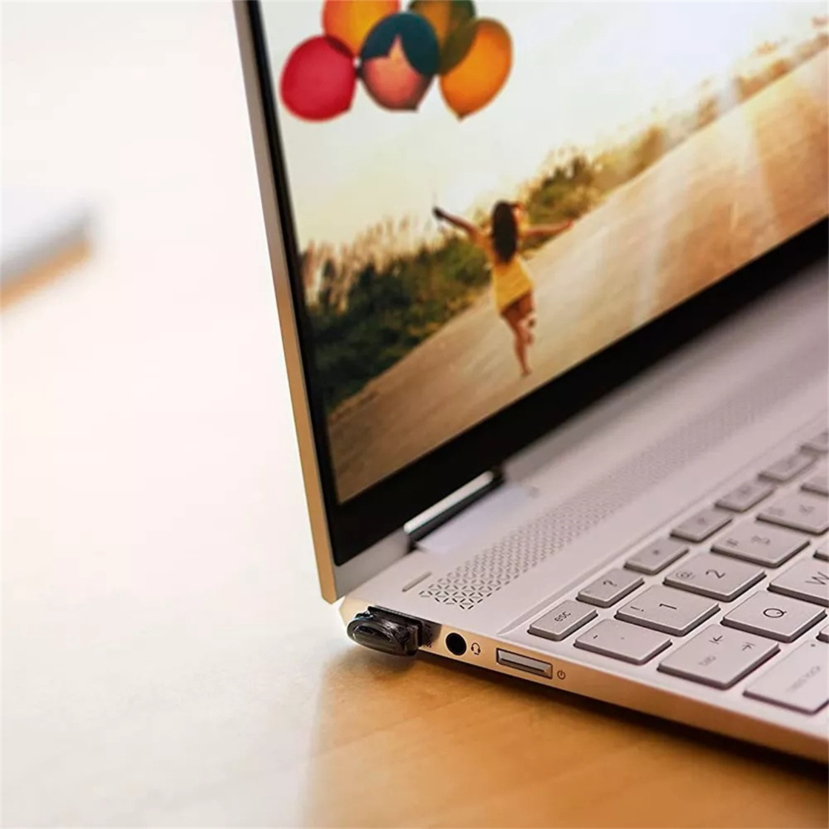 Laptop-Bildschirm zeigt eine Frau, die mit Ballons rennt. Der Laptop steht auf einem Holztisch.