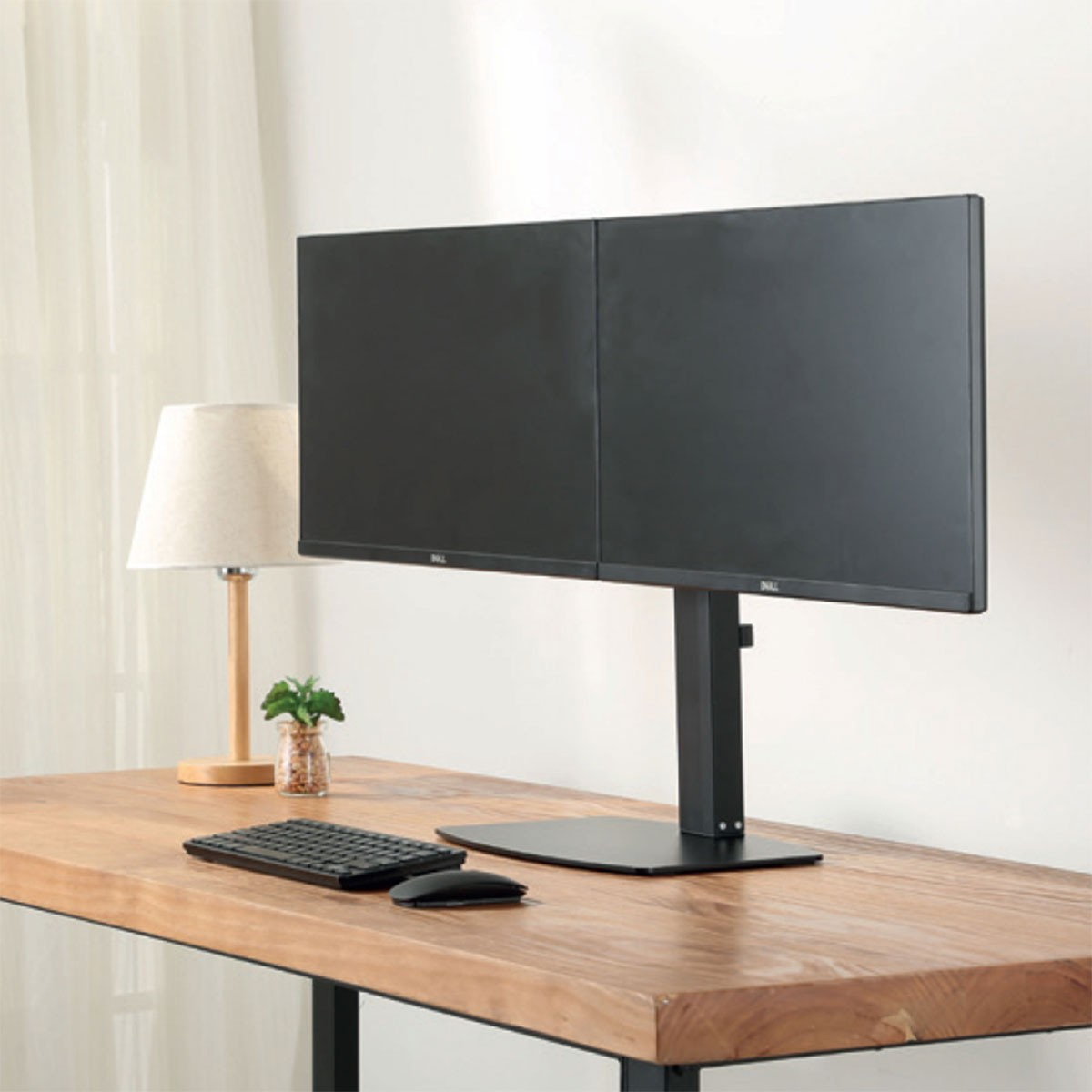 Scrivania con doppi monitor, tastiera, mouse e lampada. Superficie in legno.