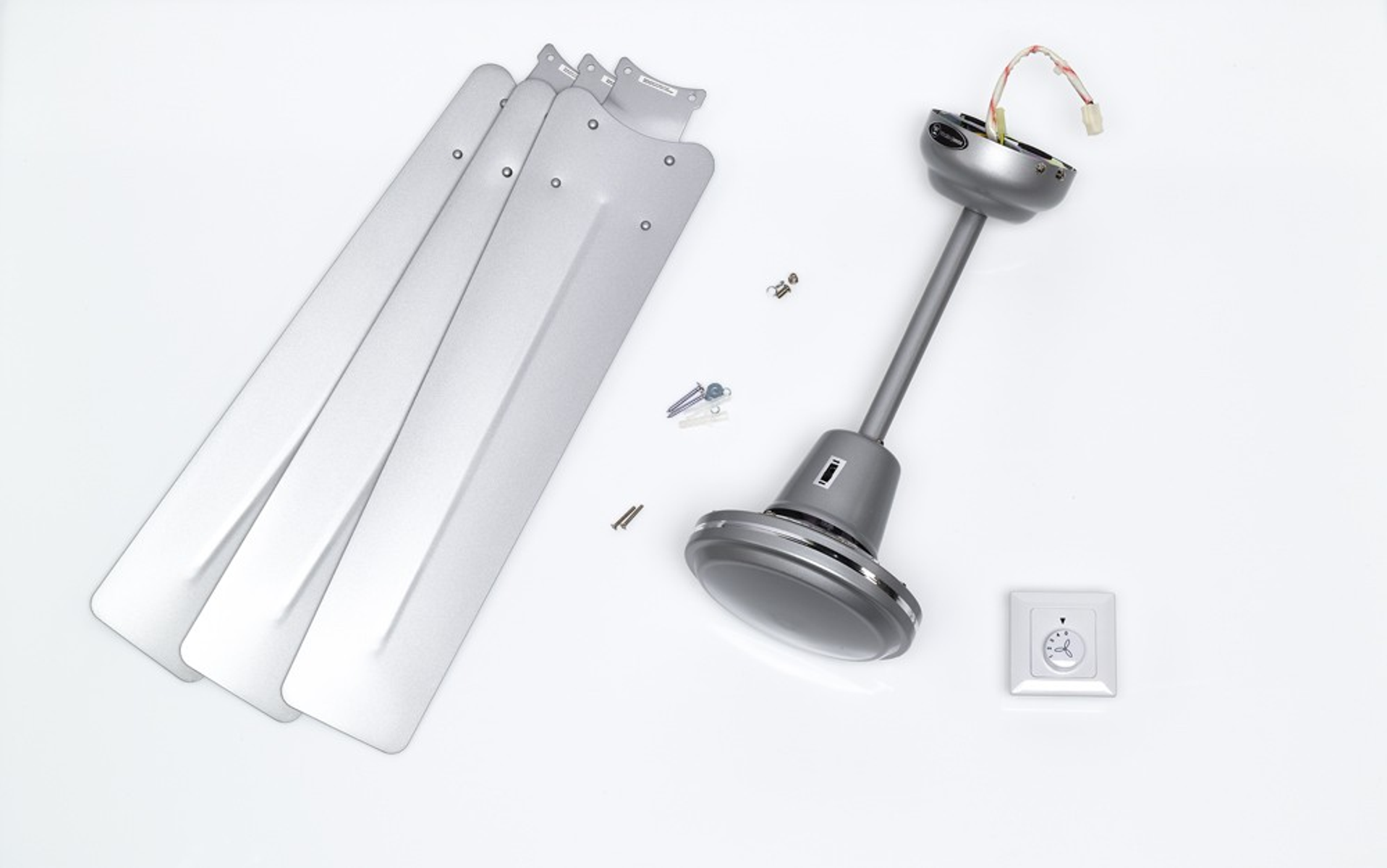 Componenti del ventilatore da soffitto smontati, tra cui pale, alloggiamento motore e telecomando su bianco.