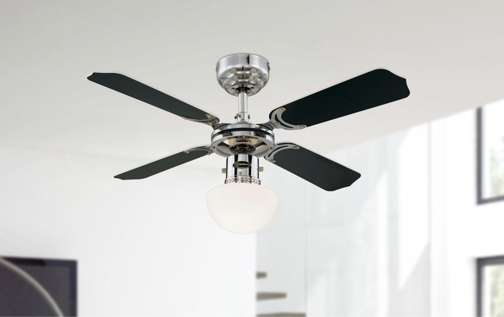 Ein silberner Deckenventilator mit schwarzen Flügeln und einer darunter hängenden Glaslampe.