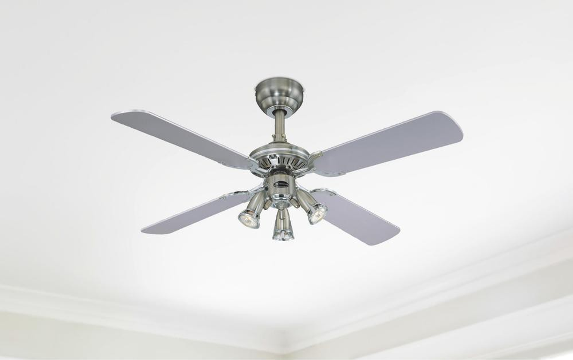 Ventilatore da soffitto con quattro pale grigie, un'attrezzatura centrale cromata e tre luci, contro un soffitto bianco.