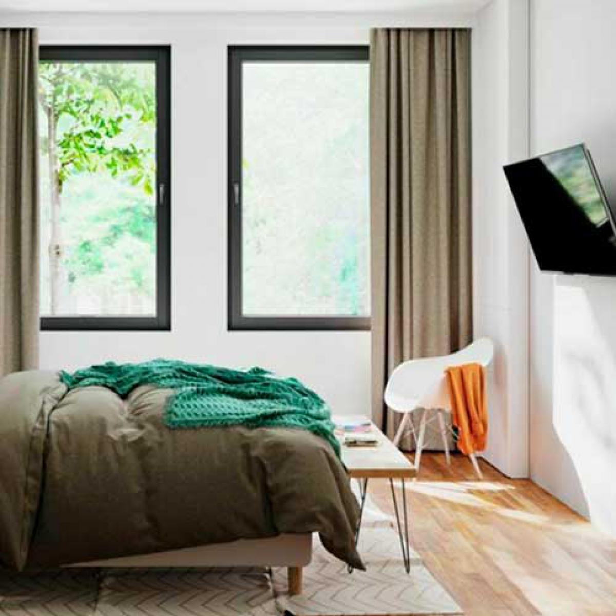 Un letto con coperta verde, due finestre e una TV.