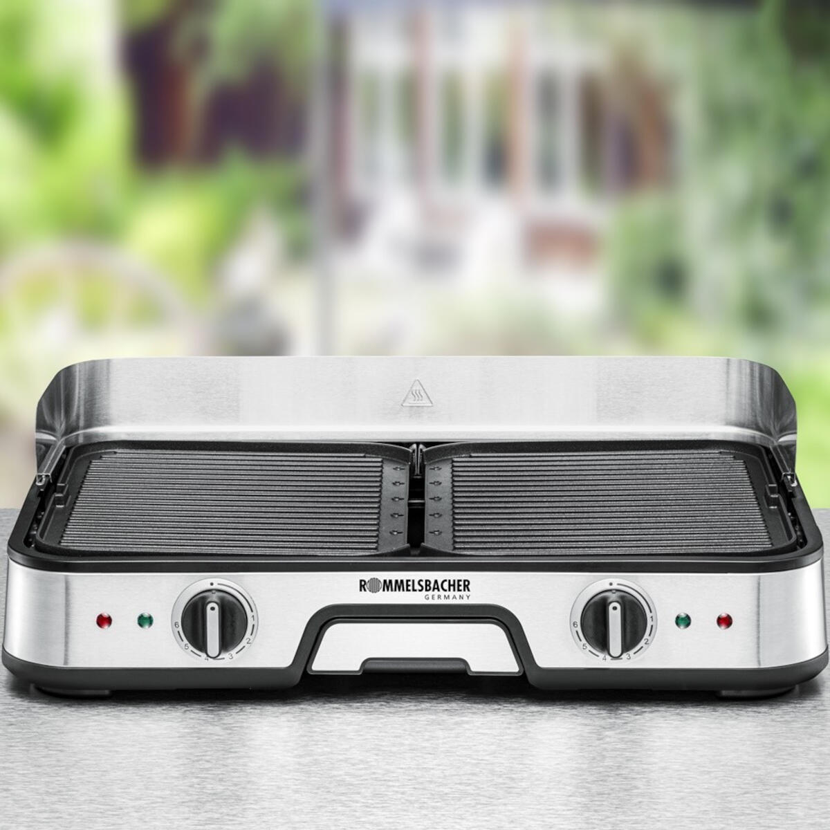 Silver and black electric grill on a light surface with a blurred background.
