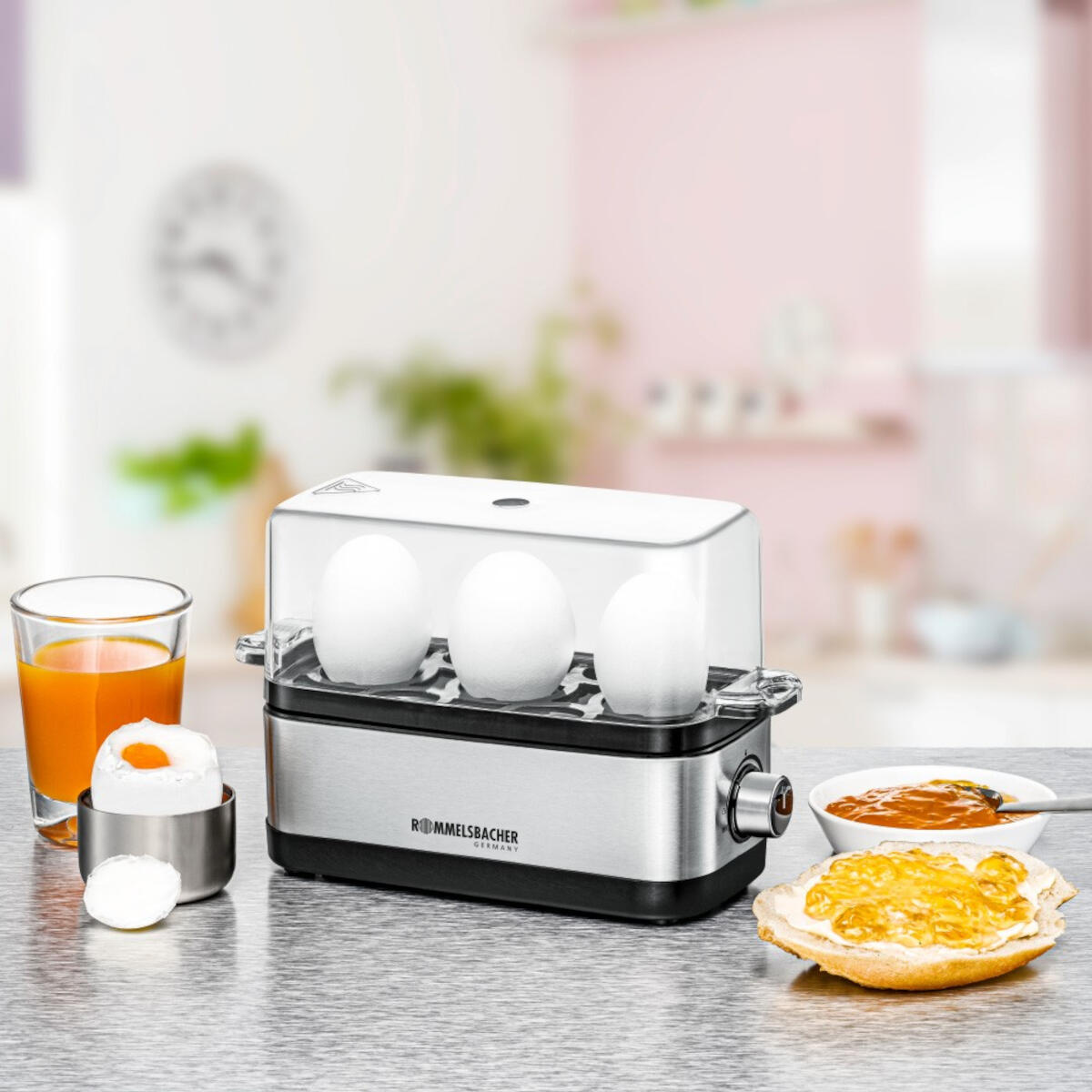 Cuiseur d'œufs avec trois œufs et des articles de petit-déjeuner sur une table, fond de cuisine.