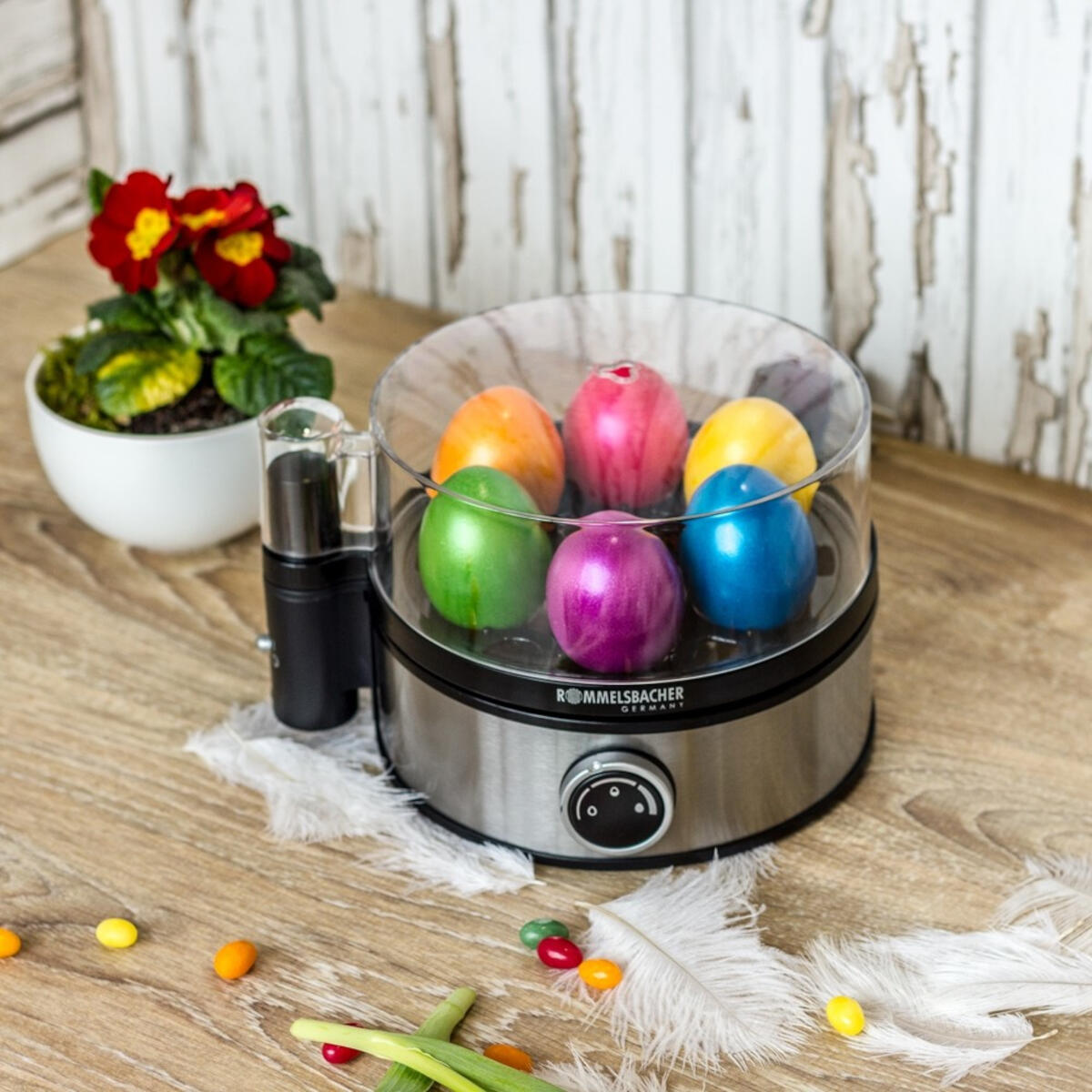 Parowar do jajek wielkanocnych z kolorowymi jajkami, kwiatami i cukierkami na drewnianym stole.