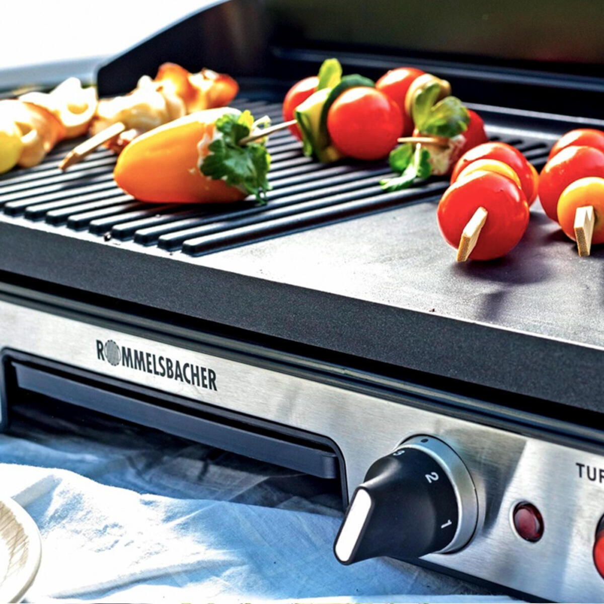 Un grill avec de la nourriture cuite, y compris des brochettes et des légumes, et un bouton de commande.