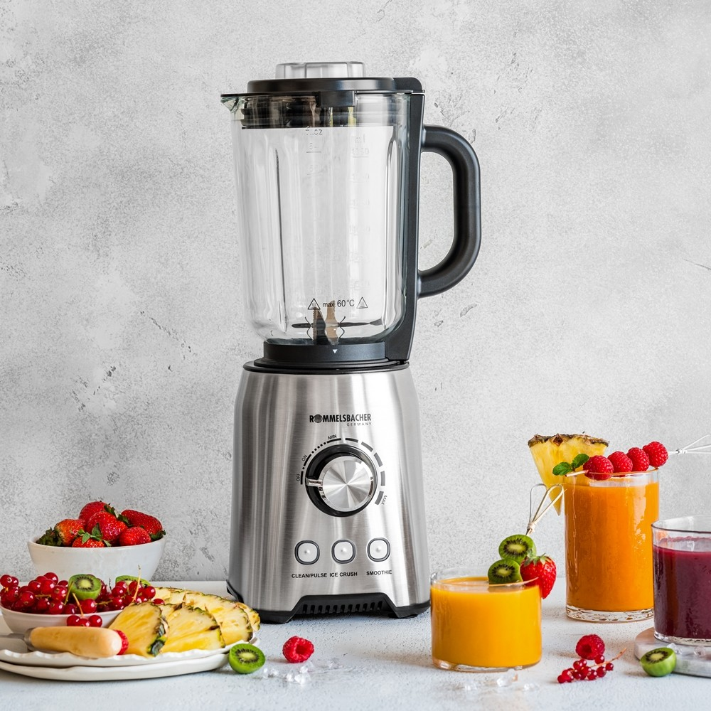 A silver blender sits on a white surface with fruit and juice glasses. Light grey background.