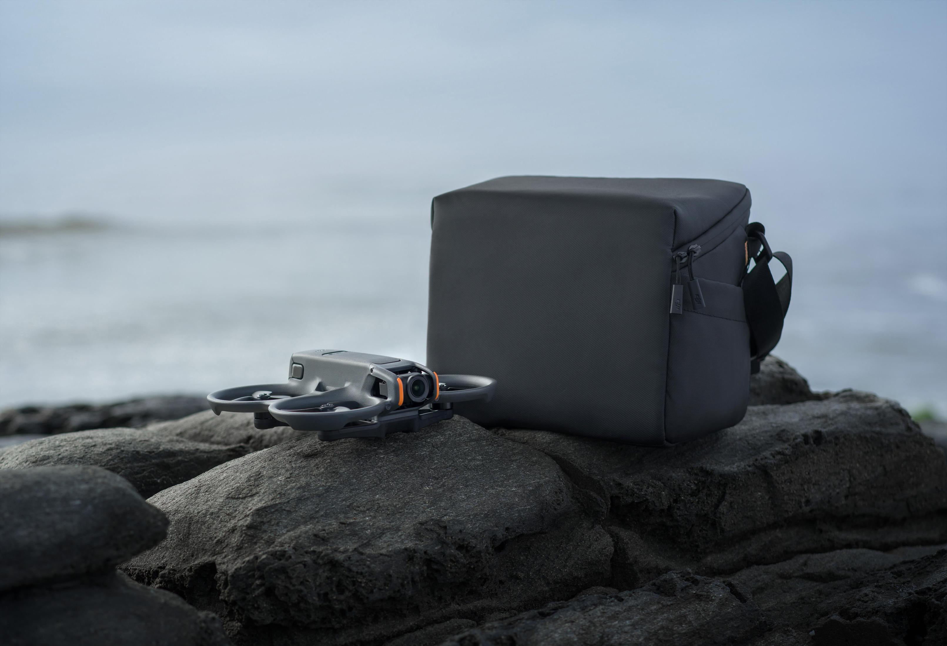 Dron i czarna torba na skale w pobliżu wody. Niebo jest zachmurzone.