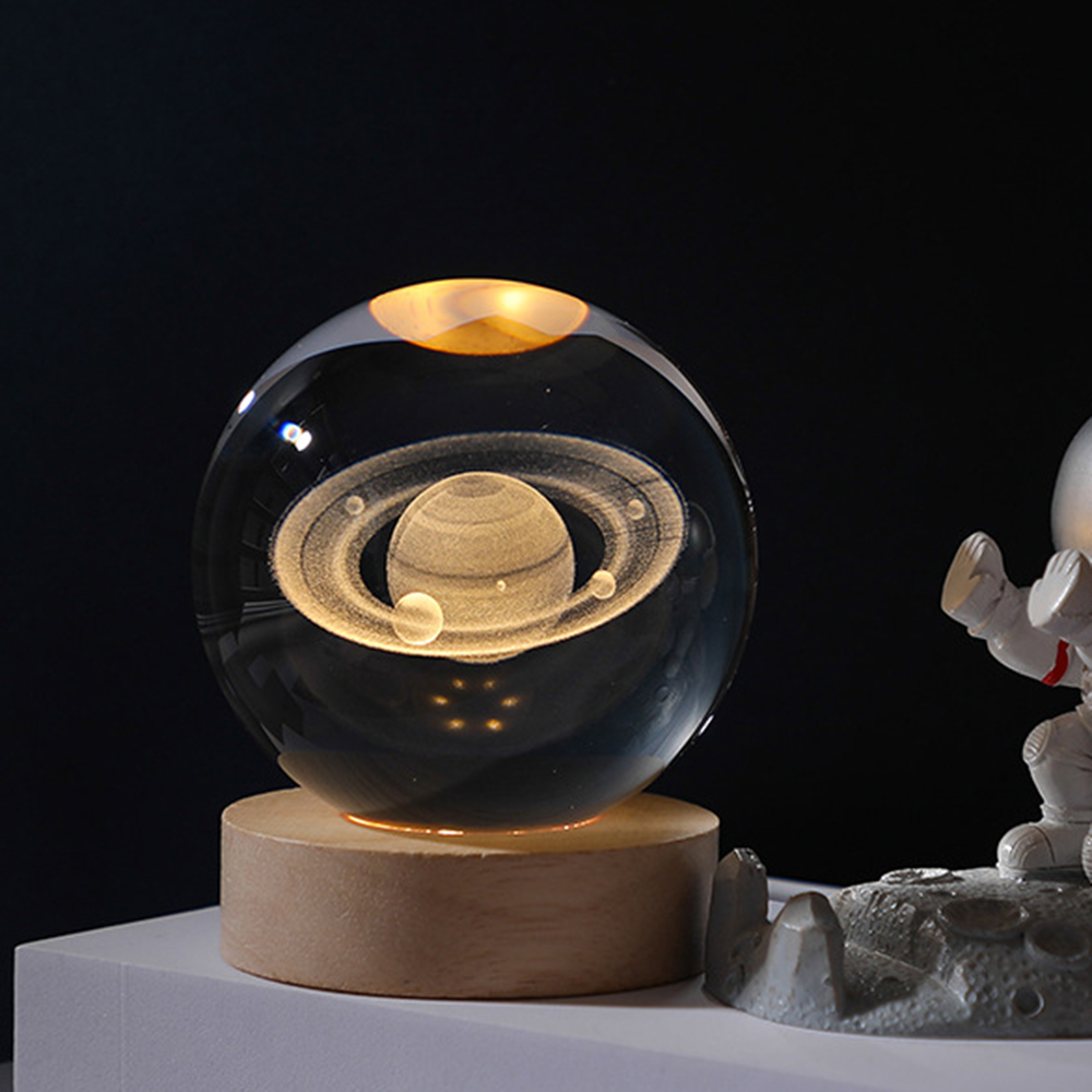 Glaskugel mit Saturnmodell, auf Holzsockel, mit Astronautenfigur.