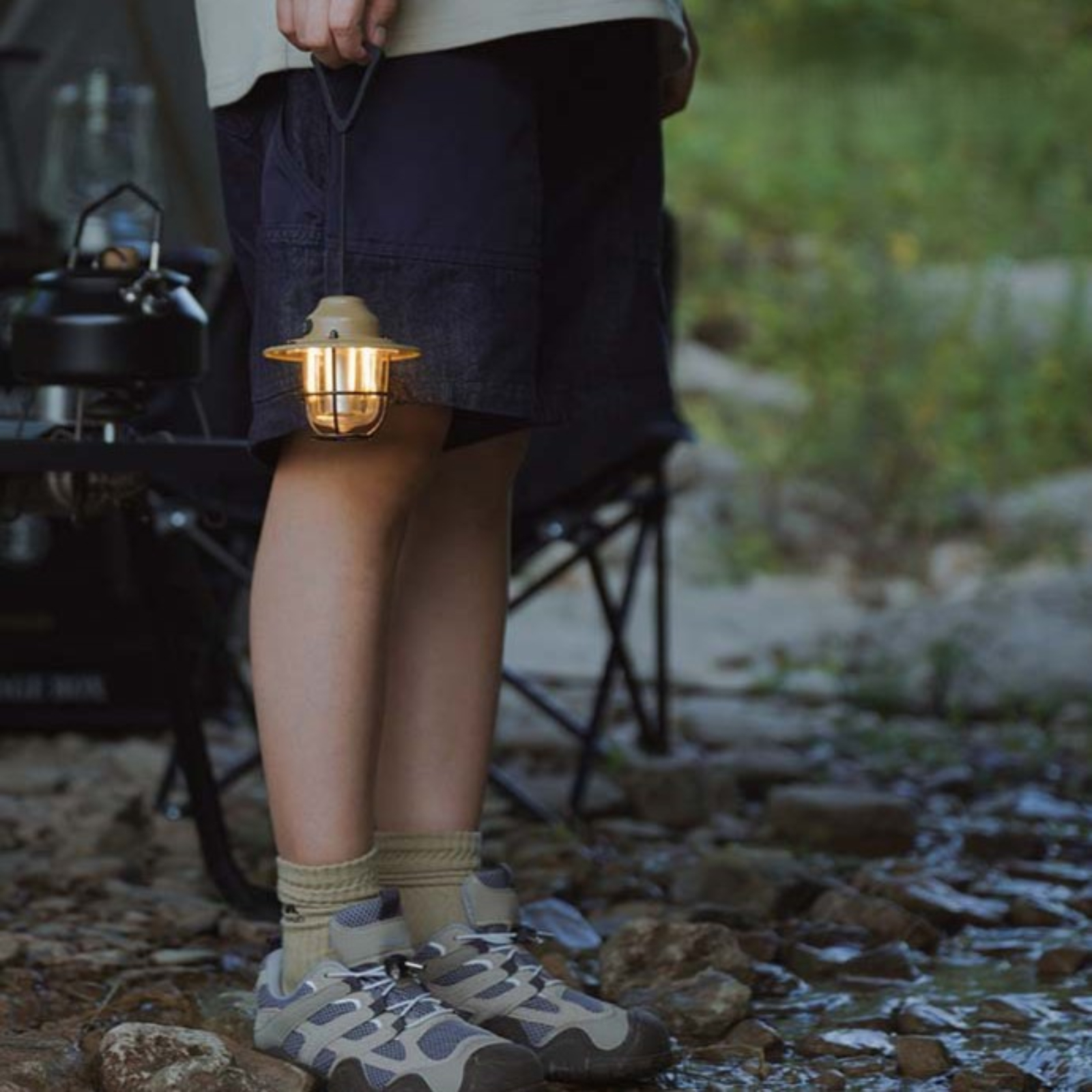 Eine Person mit Shorts, die eine Laterne im Vintage-Stil in einer Waldlandschaft hält.