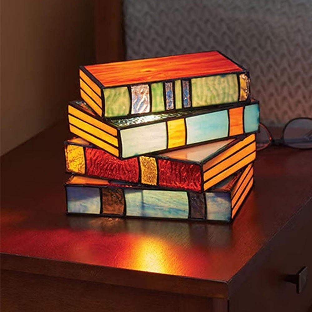 Stapel von vier beleuchteten buchförmigen Lampen auf dunkler Oberfläche. Brille daneben.