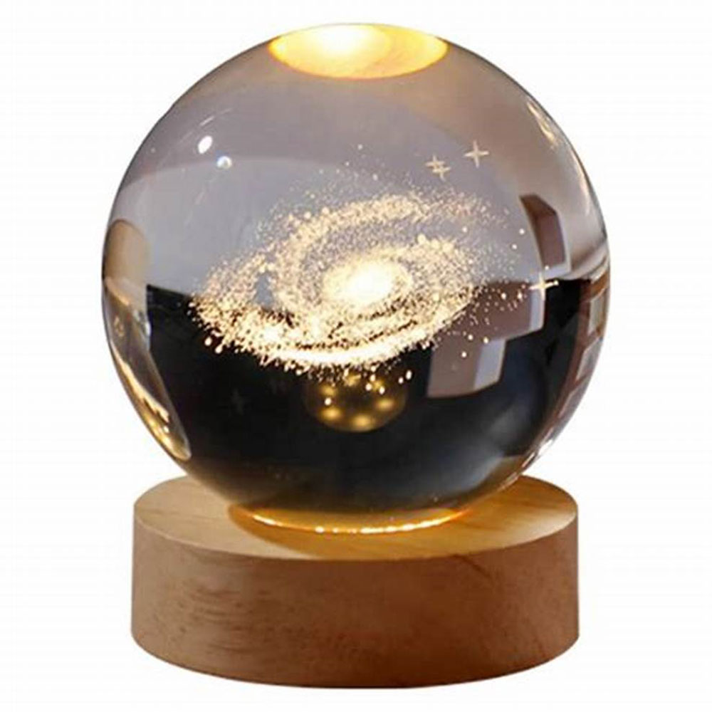 Eine Glaskugel mit einem Galaxienbild auf einem Holzsockel, von unten beleuchtet. Weißer Hintergrund.