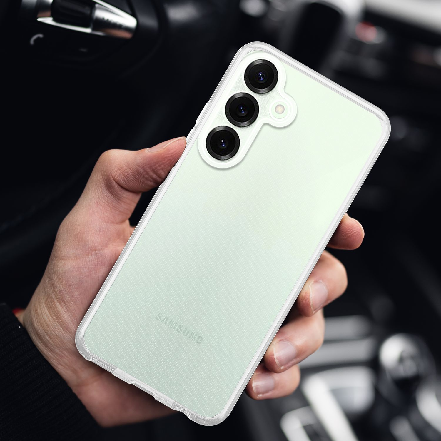 Hand hält ein hellgrünes Telefon mit drei Kameras in einer durchsichtigen Hülle, verschwommener Hintergrund.